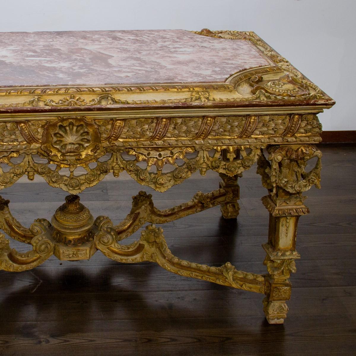 A grand Louis XIV style, red painted and giltwood ‘table de milieu’ meaning middle table, with highly decorative carvings comprising of floral swags, leaves and shells to the sides and legs which are joined by an eventful swag ‘X’ stretcher. The top