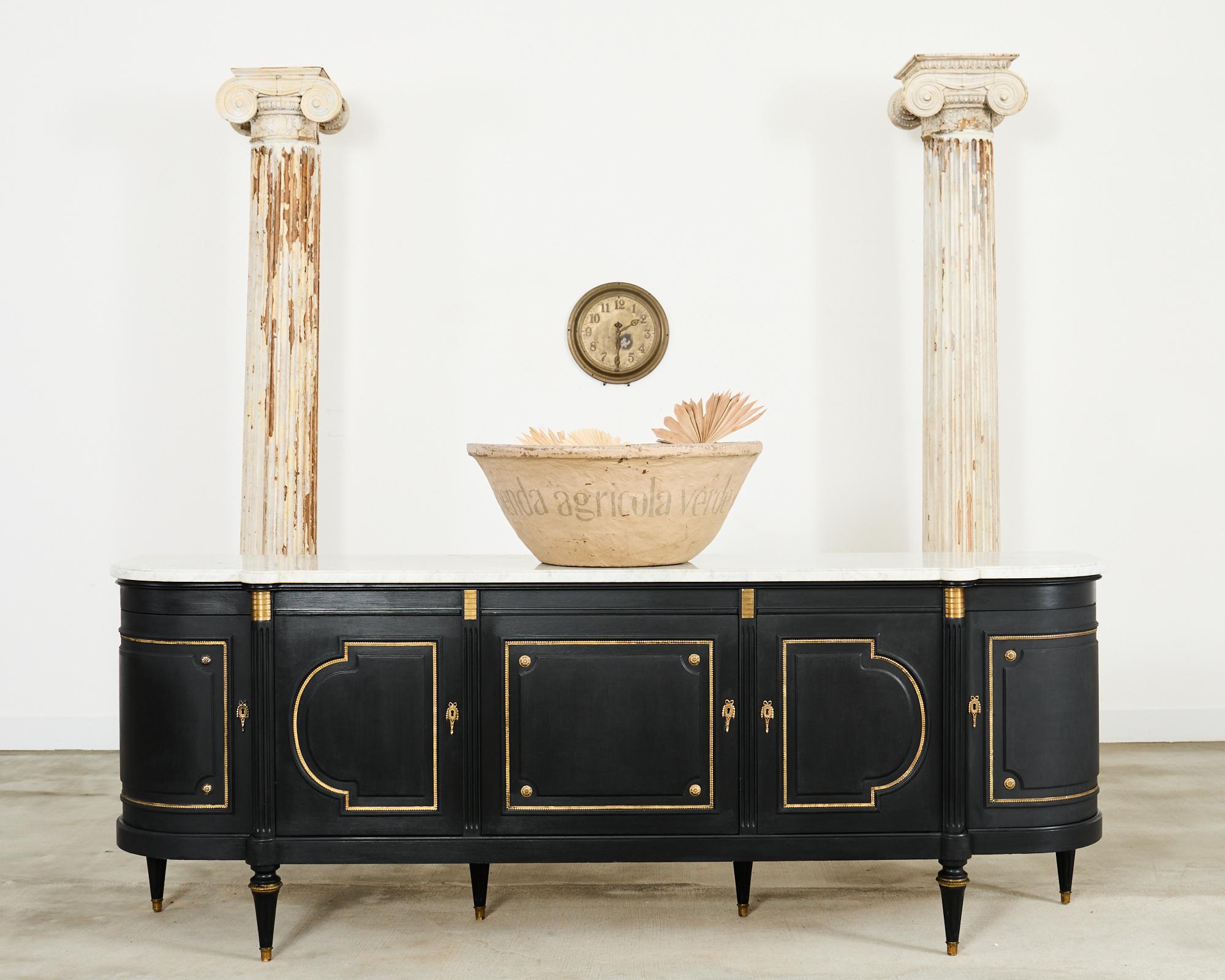 Dramatic grand French ebonized sideboard or buffet featuring a thick Carrara marble top slab. Beautifully crafted on a massive scale in the neoclassical Louis XVI taste. The case has gracefully curved demi-lune ends with five storage doors opening