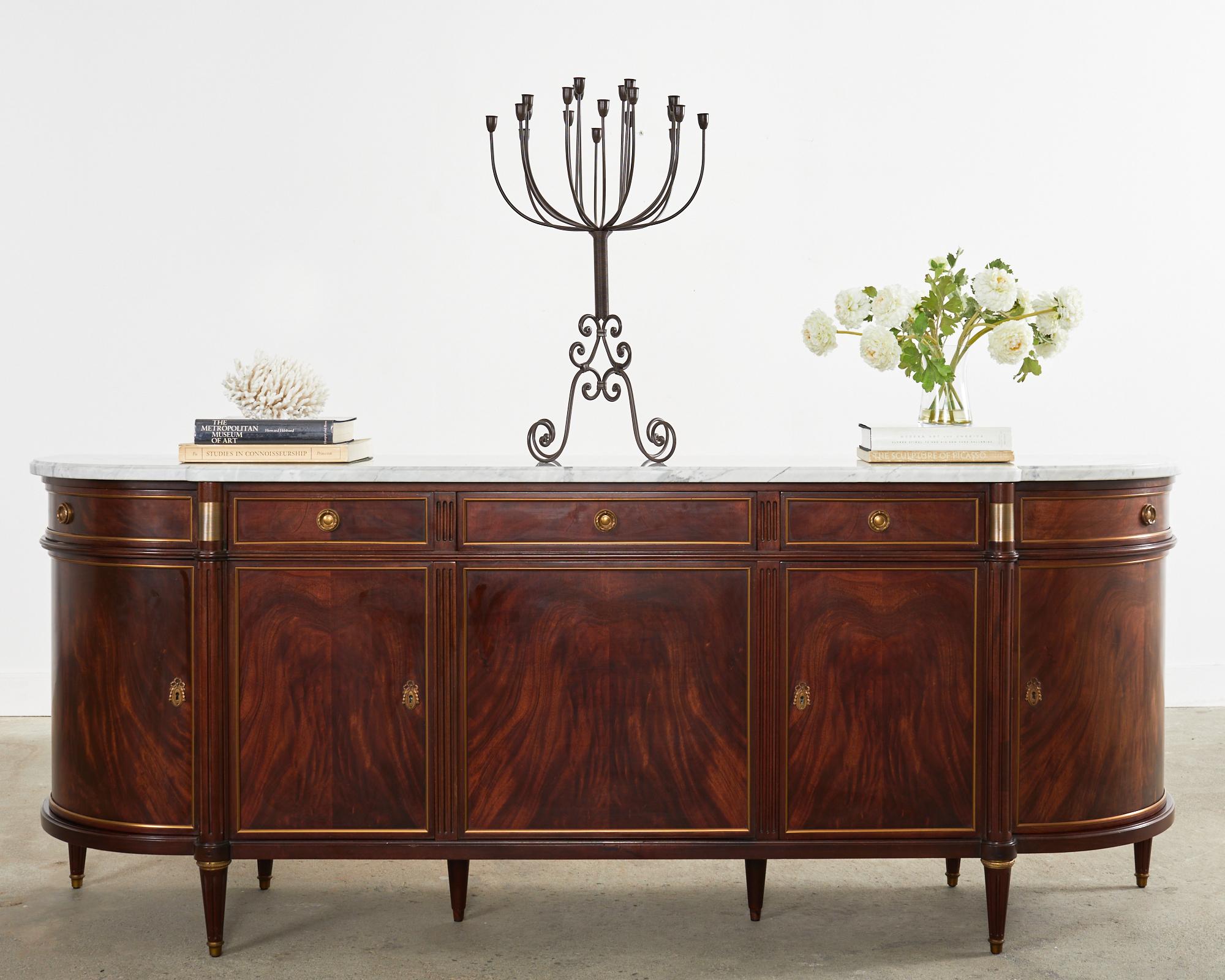 Grand French mahogany sideboard or buffet server featuring a thick Italian Carrara marble top. Beautifully crafted in the neoclassical Louis XVI taste by French artisan cabinet makers. The mahogany case has classic French curved demilune ends with