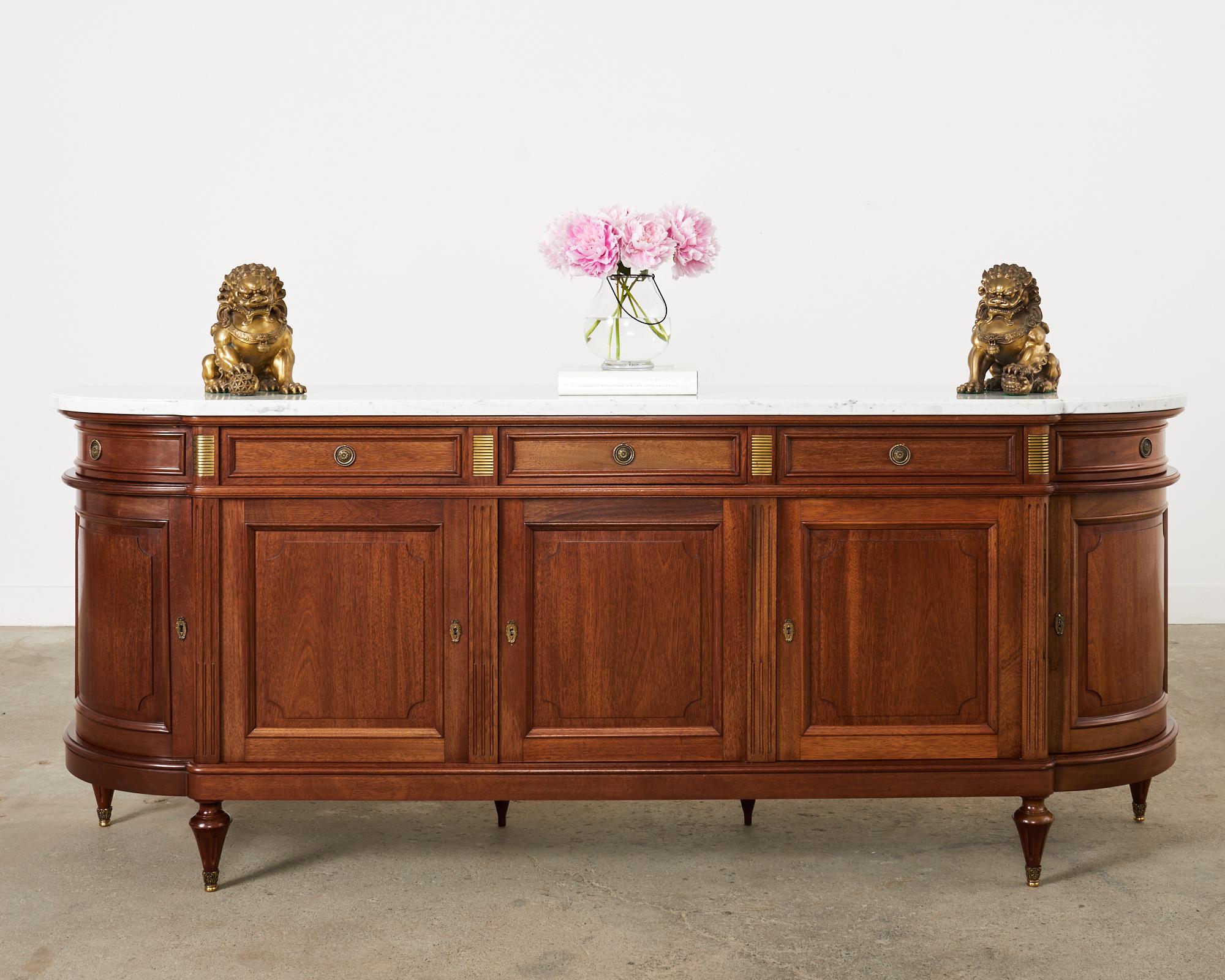 Grand French mahogany sideboard buffet or server featuring a massive Italian Carrara marble top. Beautifully crafted in the neoclassical Louis XVI taste by French artisan cabinet makers. The mahogany case has classic French curved demilune ends with