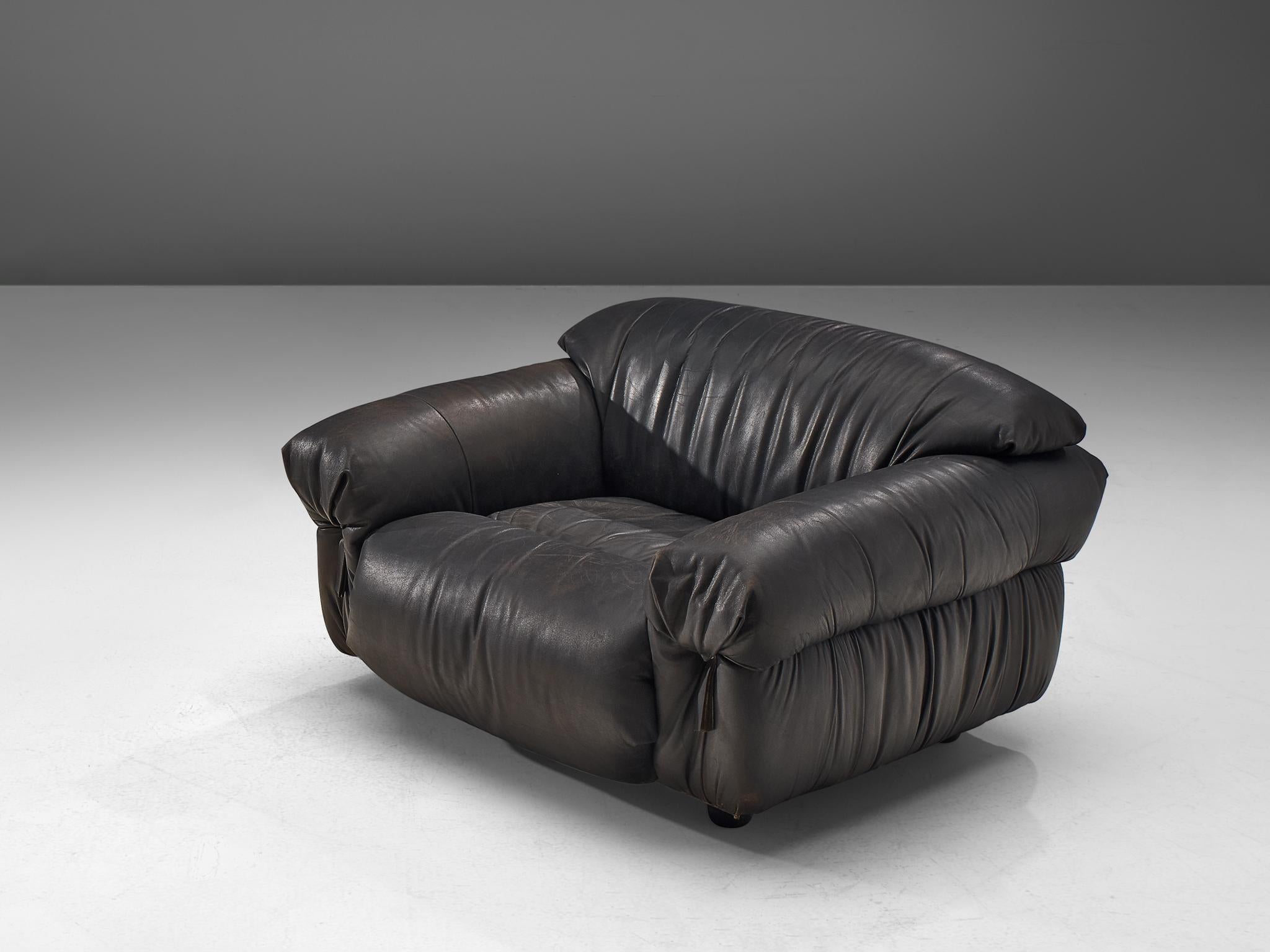 Lounge chair, leather, Italy, 1970s.

Grand and bulky lounge chair. Completely covered in high-quality, thick leather that patinated beautiful over the years. The draped and folded leather is finished with leather straps at the front of the