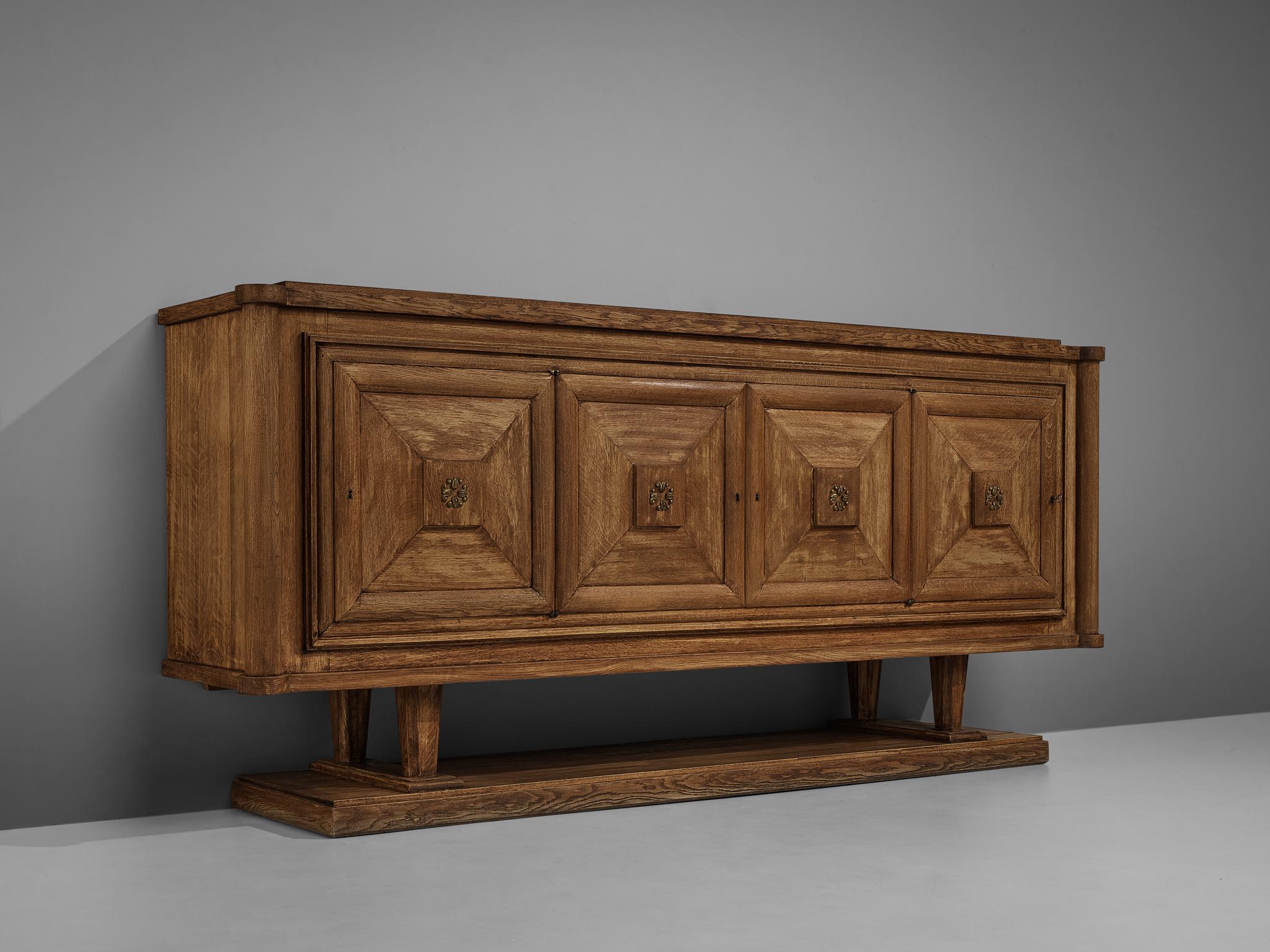 Sideboard, oak, brass, France, 1950s

Grand art deco sideboard with four graphical doors. This expressive credenza features striking woodwork. The doors are structured with geometric forms, the center is highlighted with ornaments in brass. An