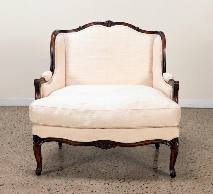 Grand Proportioned Louis XV Style Bergeré Armchair and Ottoman. Very comfortable. Carved walnut frame with shaped cabriole legs. Small stains on parts of the fabric - reupholstery recommended. Early 20th Century. 
Measures: 37.5” H 38.25” W 32.25”