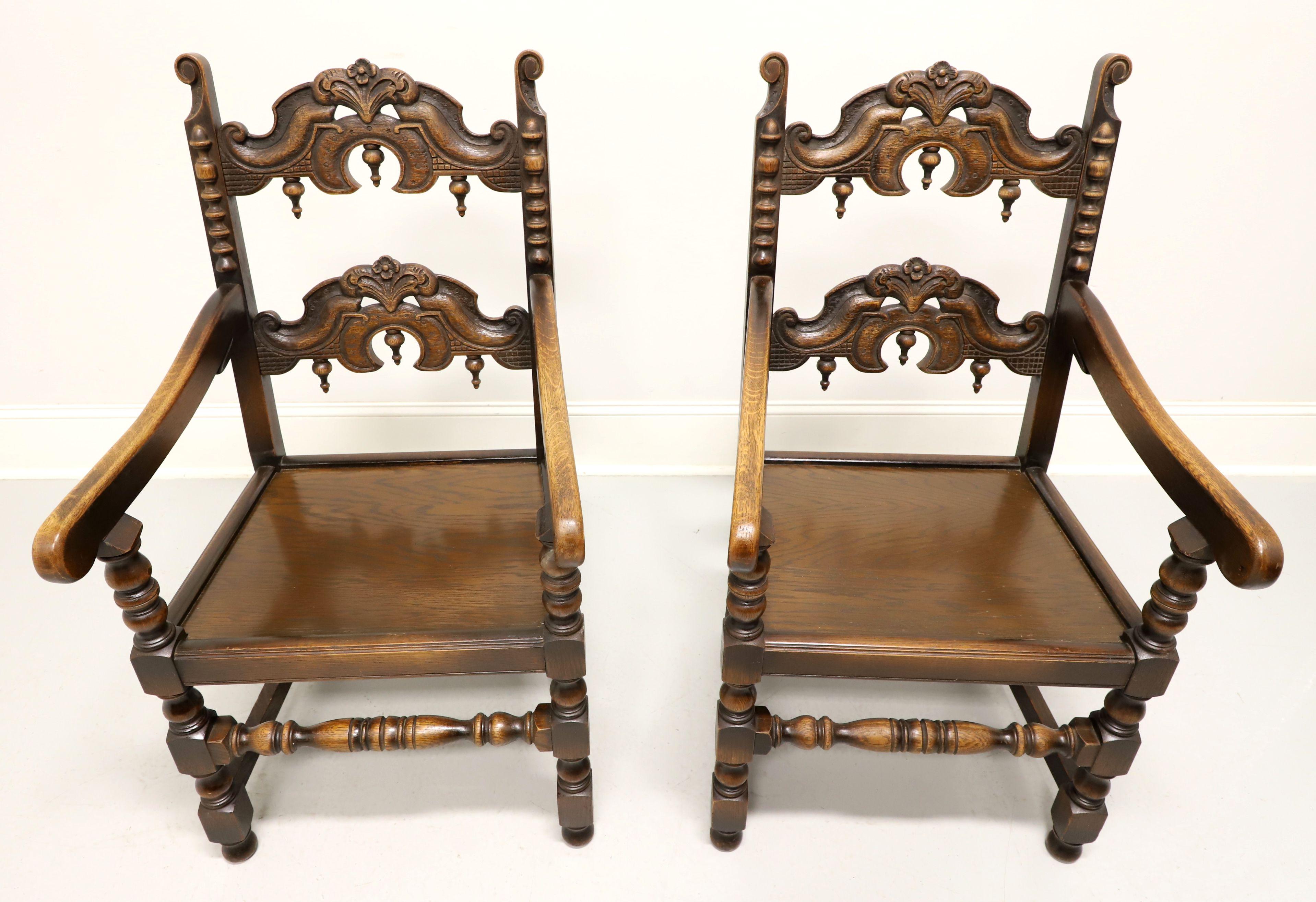 An antique pair of Gothic Revival style dining armchairs by Grand Rapids Bookcase and Chair Company. Solid oak with carved and turned details. Features a decoratively carved ladder back with inverted finials, carved stiles, sloped curved arms with