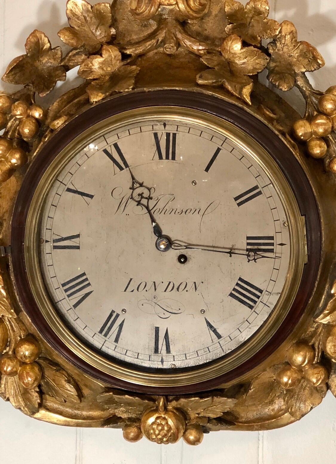 Important English Regency giltwood wall mounted clock having mahogany ring holding the convex glass door with molded brass bezel. The twelve inch engraved silvered dial is signed Wm. Johnson, LONDON. The clock hands are blued steel. The clock has an