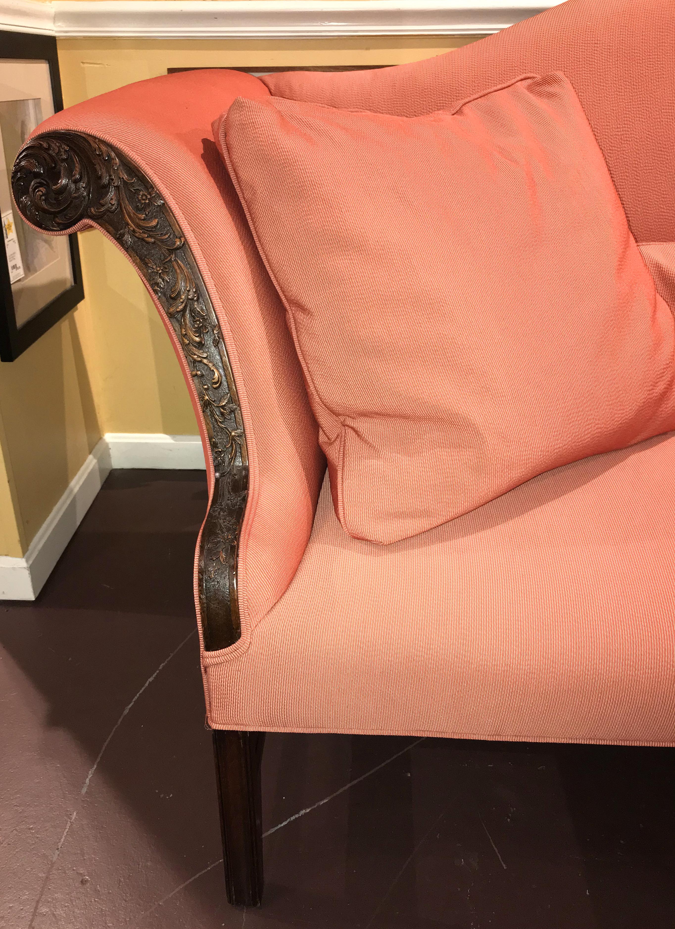 A fine grand scale Georgian mahogany camelback sofa with beautiful foliate carved arms, recently upholstered in a muted salmon color, supported by eight legs, the front with molded square legs, and the back with outswept square legs. A central