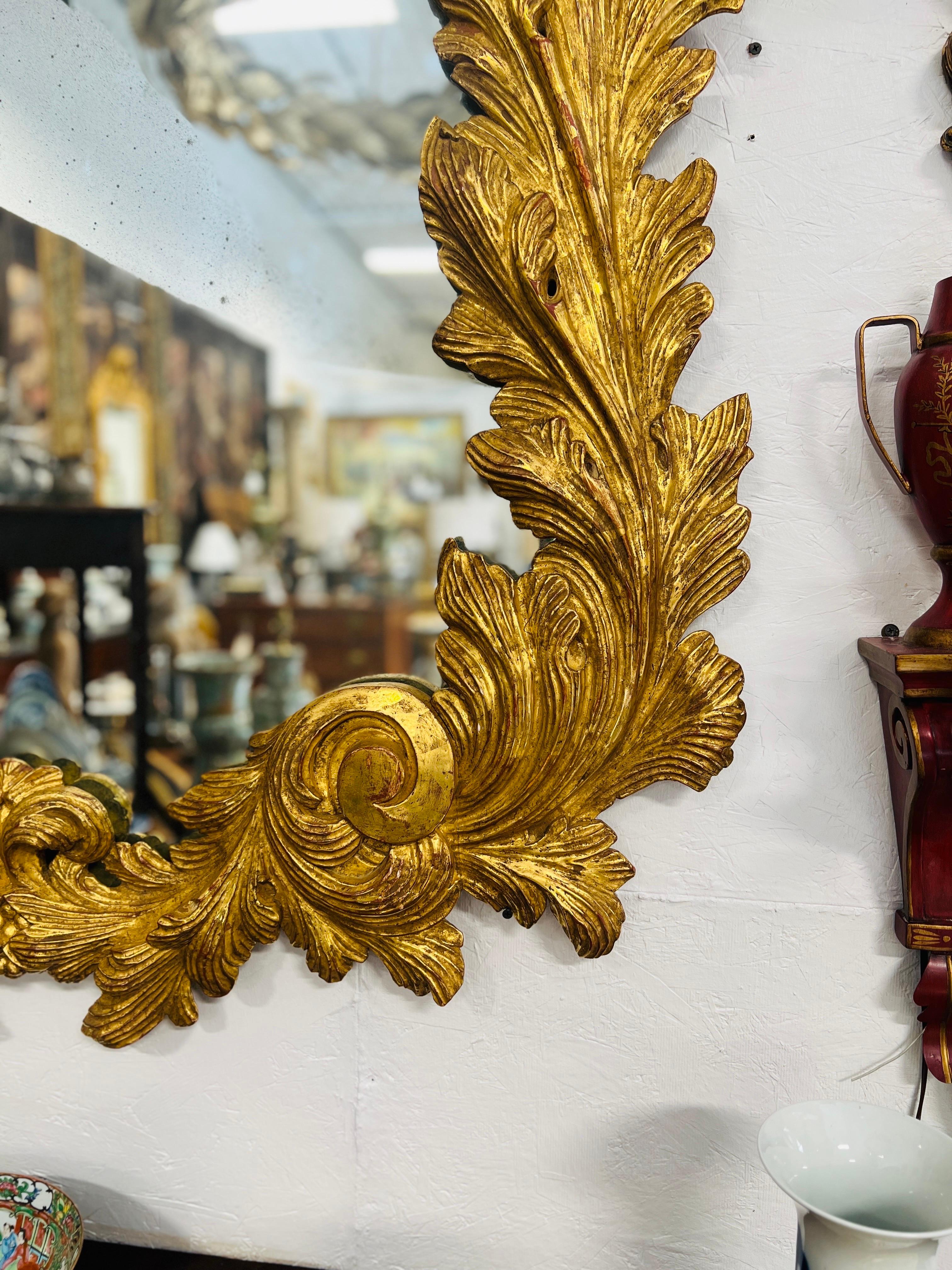 A phenomenal Italian made gilt wood mirror. Sizable frame with fine and intricate carvings in the Rococo taste. Acanthus and foliate leaf edges encompass the carved borders, scrolling details, ‘antiqued’ glass and original gold leaf make this mirror
