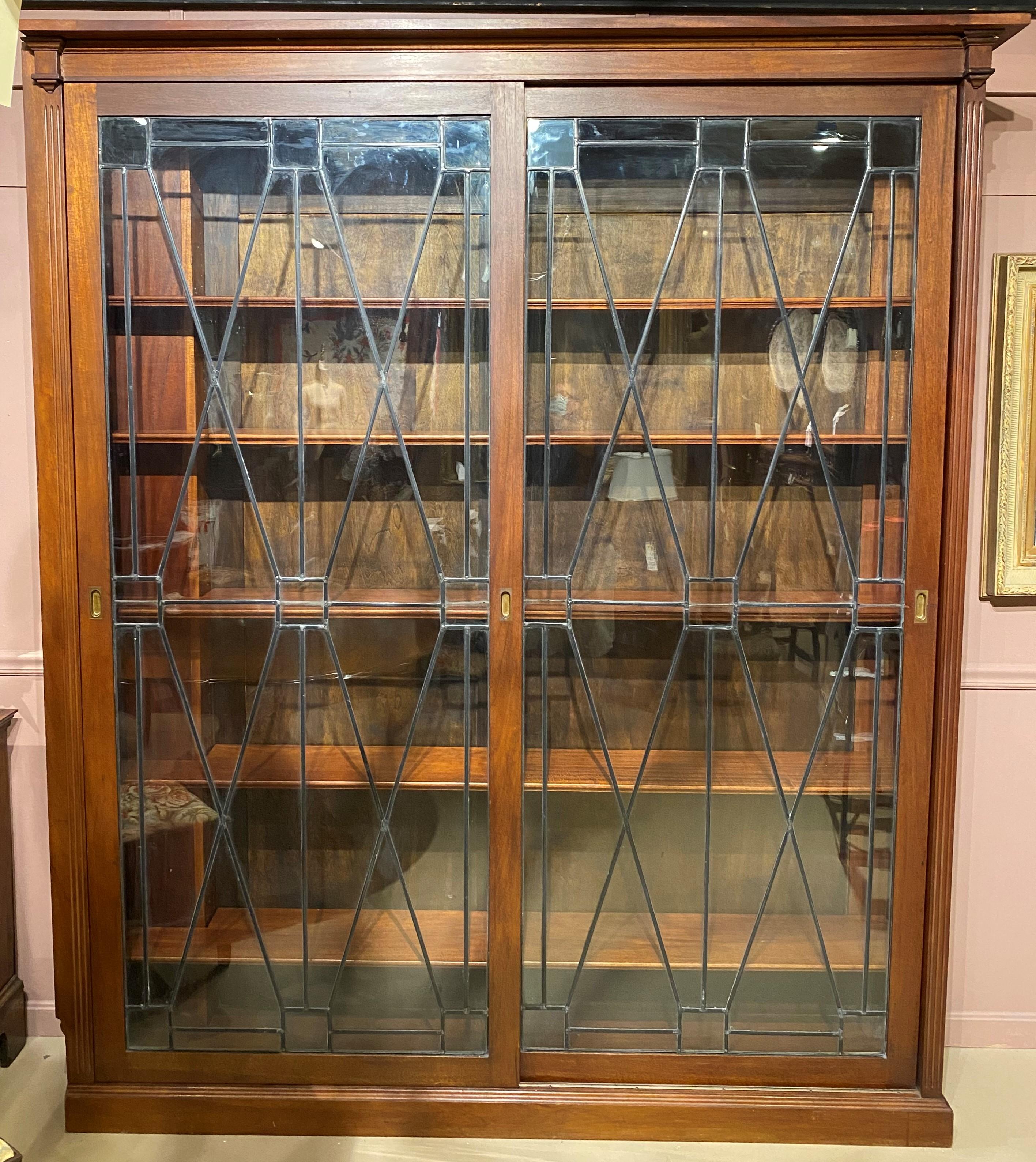 A fine large two-door bookcase with sliding leaded glass doors and adjustable shelves, originally a built-in floor to ceiling piece, with a cut-in on the left side, built around heating pipes in the building. The top would have had molding that was