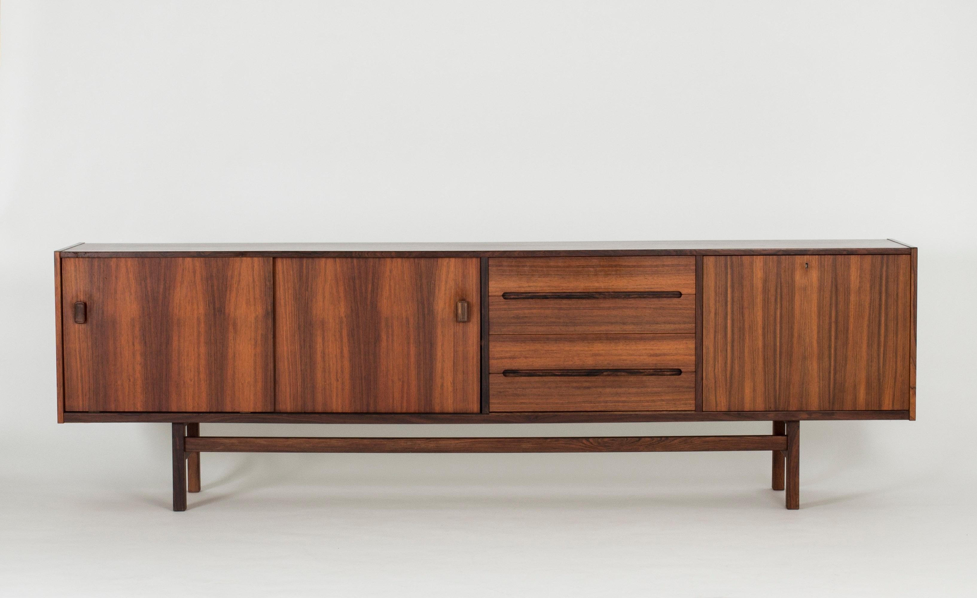 Striking rosewood sideboard by Nils Jonsson. Beautifully sculpted handles and veneer laid in contrasting directions. The door to the right opens up to a bar shelf inside.
