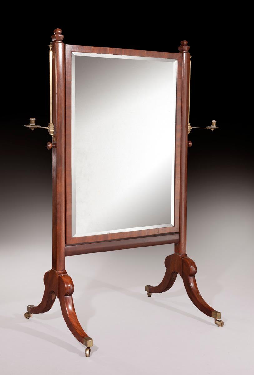A regency mahogany cheval mirror in original condition, including the bevelled plate glass and the adjustable brass candlestick holders, made in circa 1825. The solid mahogany outer frame is topped with urn shaped finials, whilst the base is raised