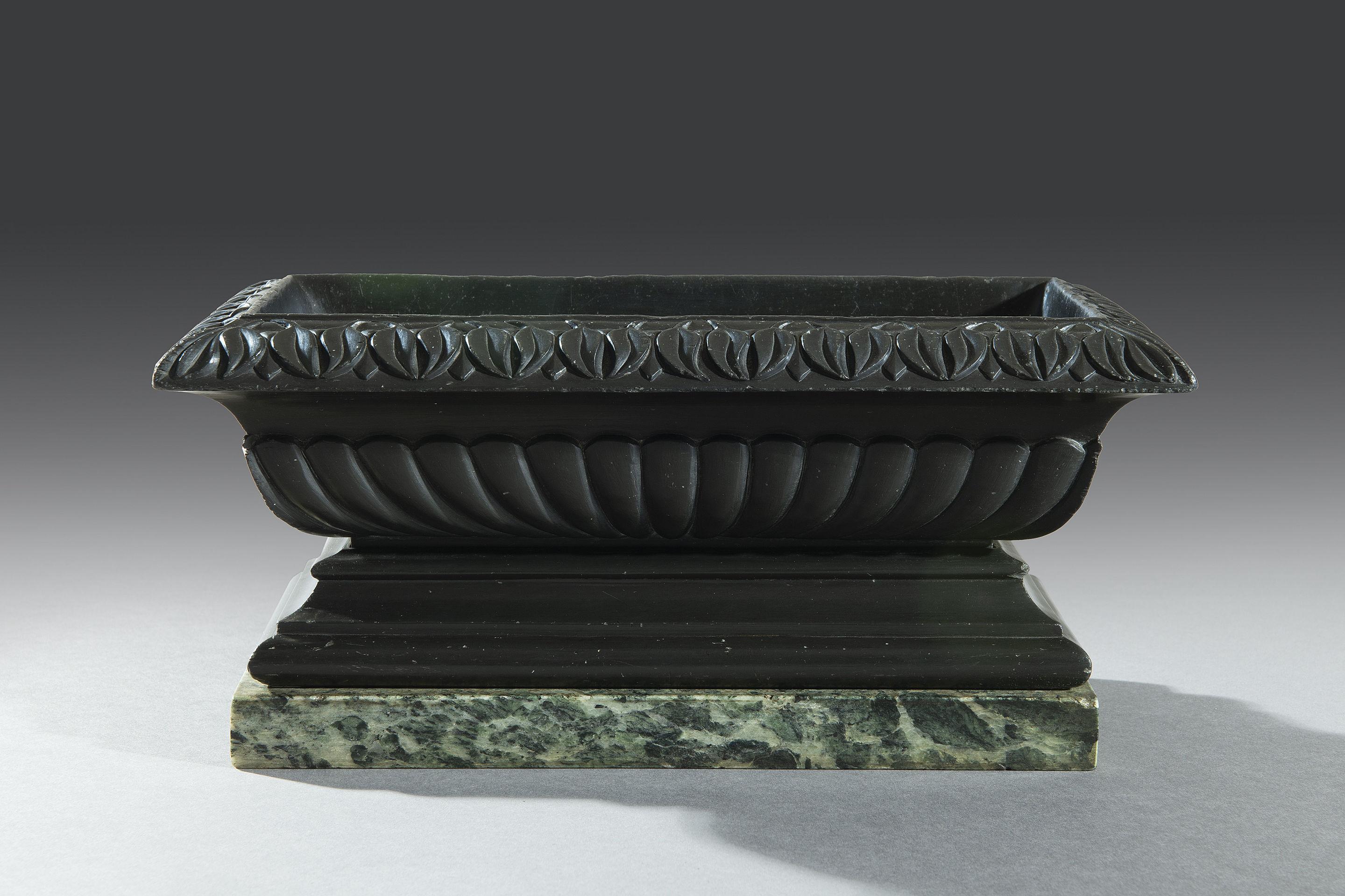 The Nero Belgio marble sarcophagus shaped bath or 'cistern' is embellished with stiff leaf borders and carved gadrooning to the body. The cistern sits a double bevelled plinth surmounted on a green marble with white quartz veins. The marble plinth