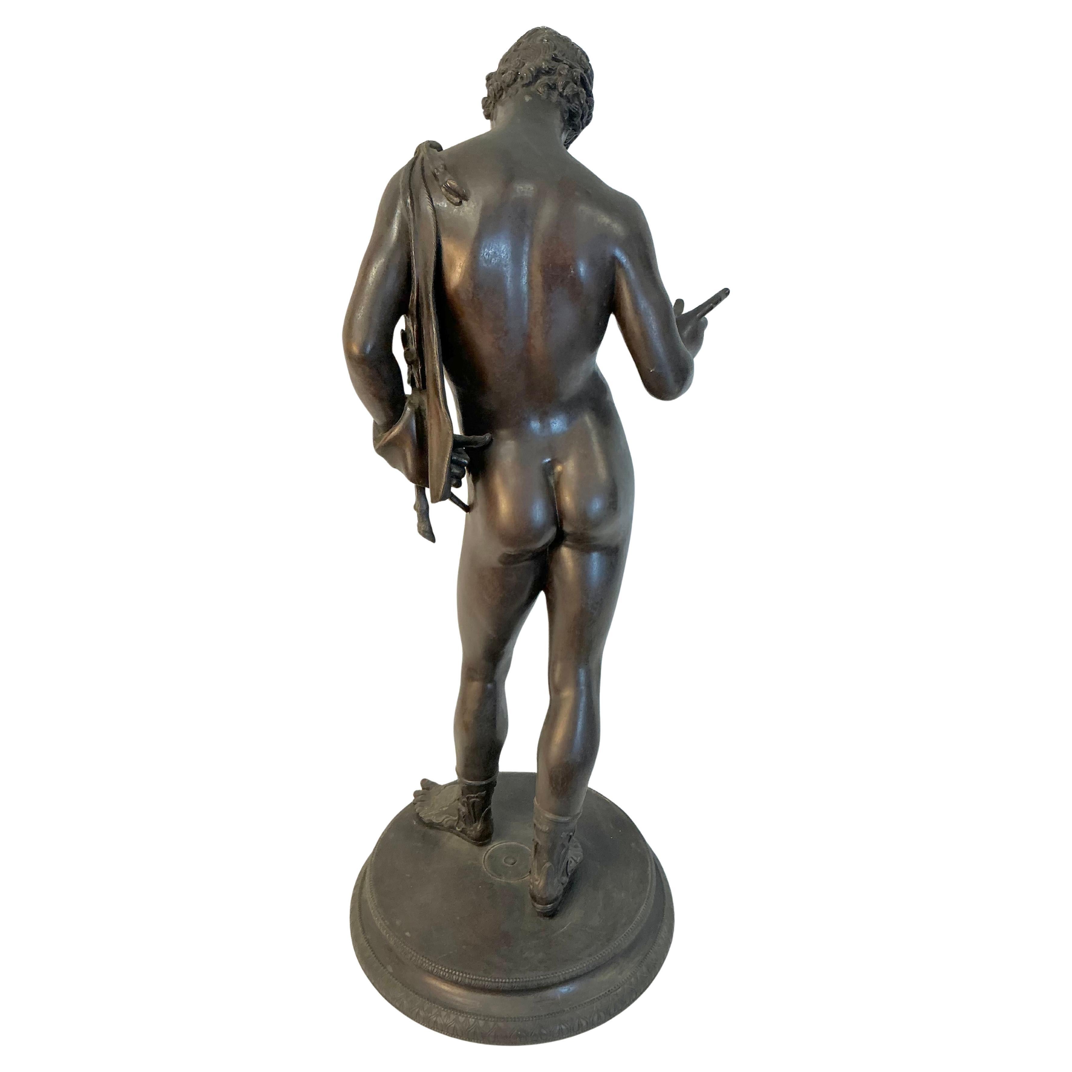 Escultura de Narciso en bronce Grand Tour del siglo XIX. Narciso aparece en un momento de autorreflexión, de pie, en una postura contemplativa. Su forma idealizada resalta su físico juvenil y atlético, centrándose en la precisión anatómica y el