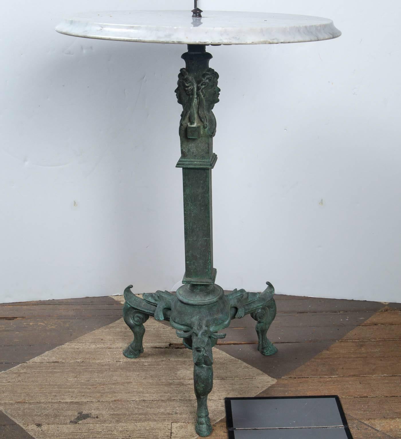 The bronze base with three animal legs with hoof feet. Above are three dolphins. To a rectangular column with two busts of Janus, atop. The white marble top, secured with a small knob finial.