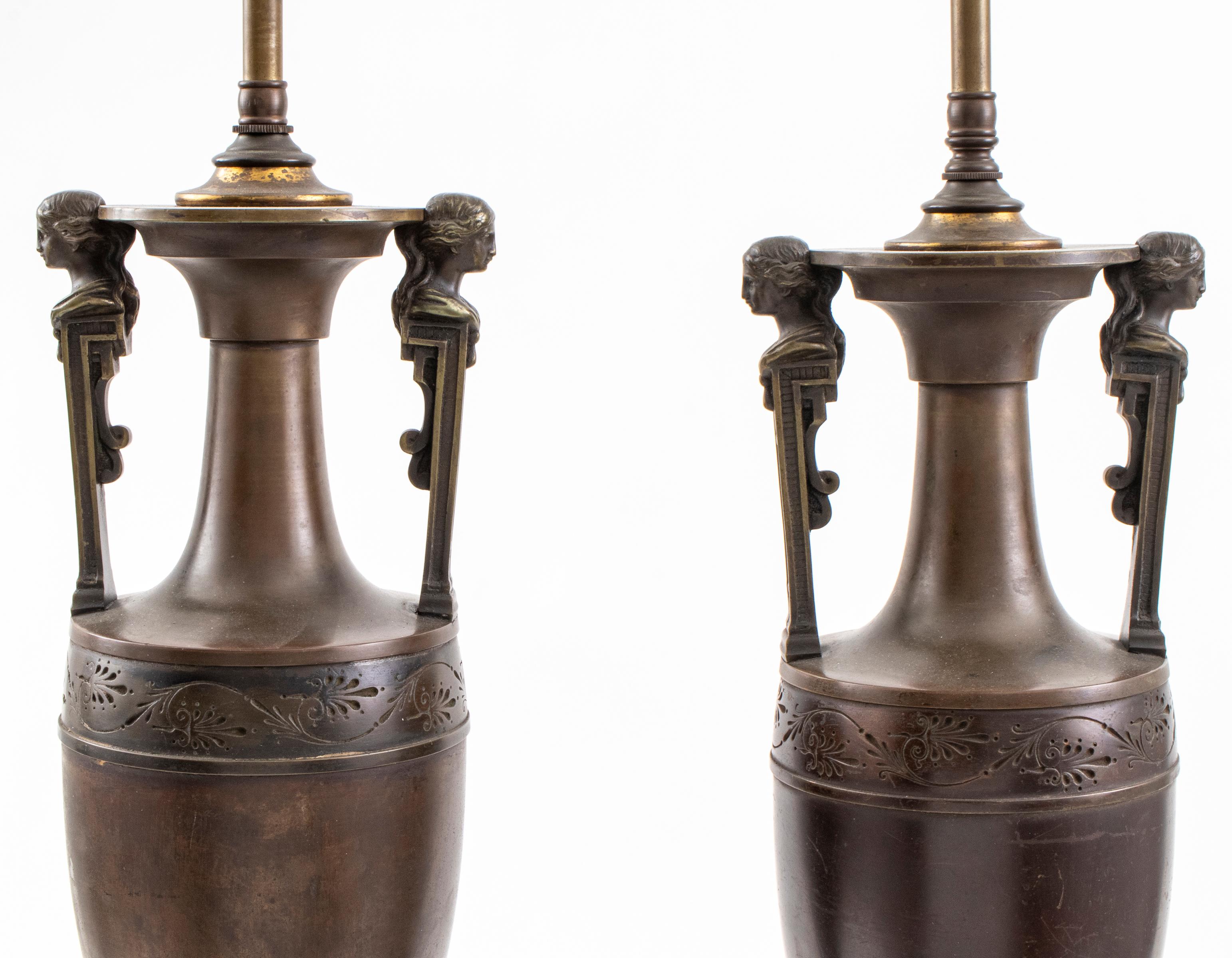 Pair of Grand Tour Etruscan Revival bronze table lamps, featuring two lights over amphora form vase, the handles modeled as female figureheads, over shaped palmette feet and mounted to associated wood base. Overall: 34.75