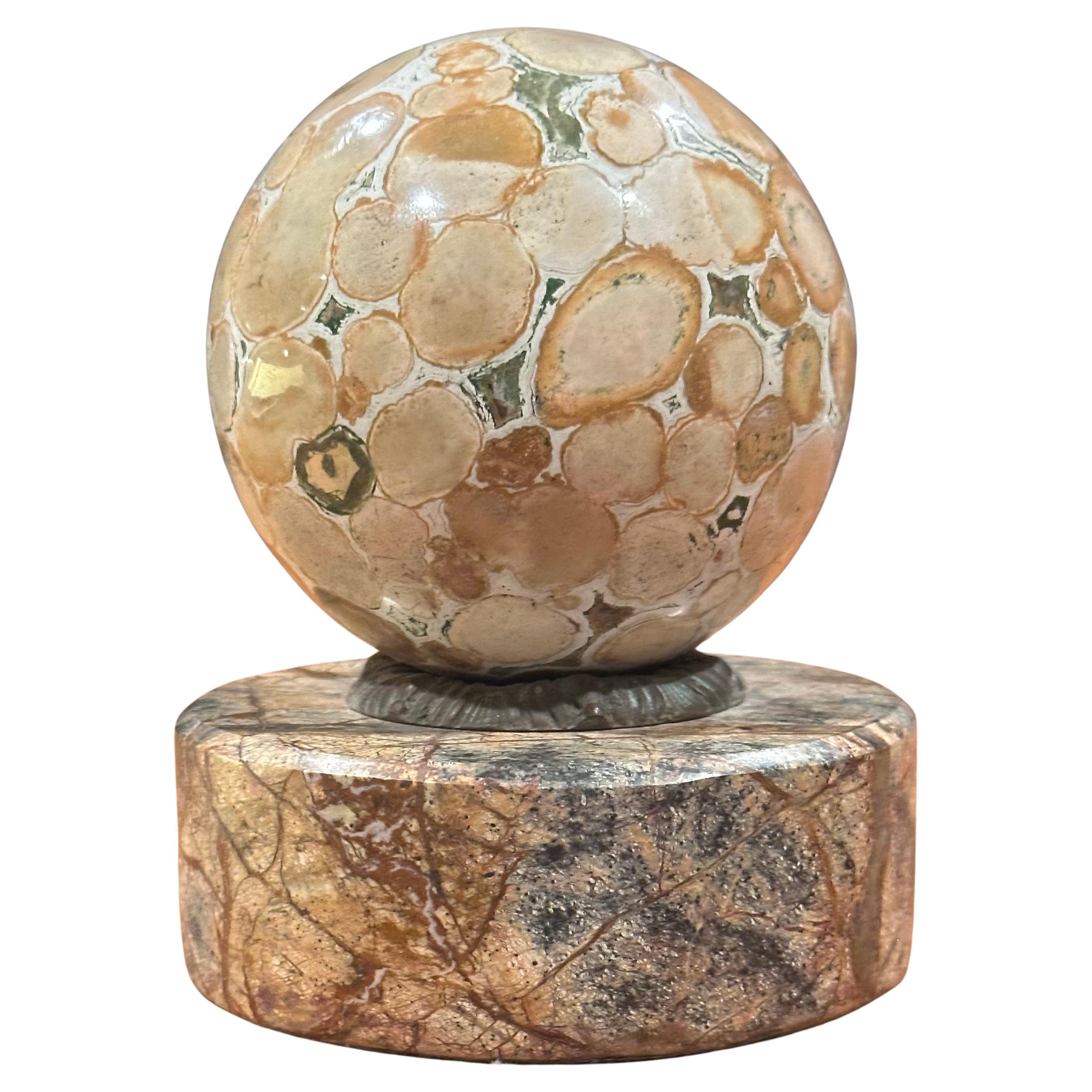 Un très beau presse-papiers en marbre grand tour sur base ronde par Theodore Alexander, circa 1995.  La pièce, qui consiste en un orbe en marbre massif assis dans un collier en bronze monté sur une base en marbre beige et brun, est en très bon état,