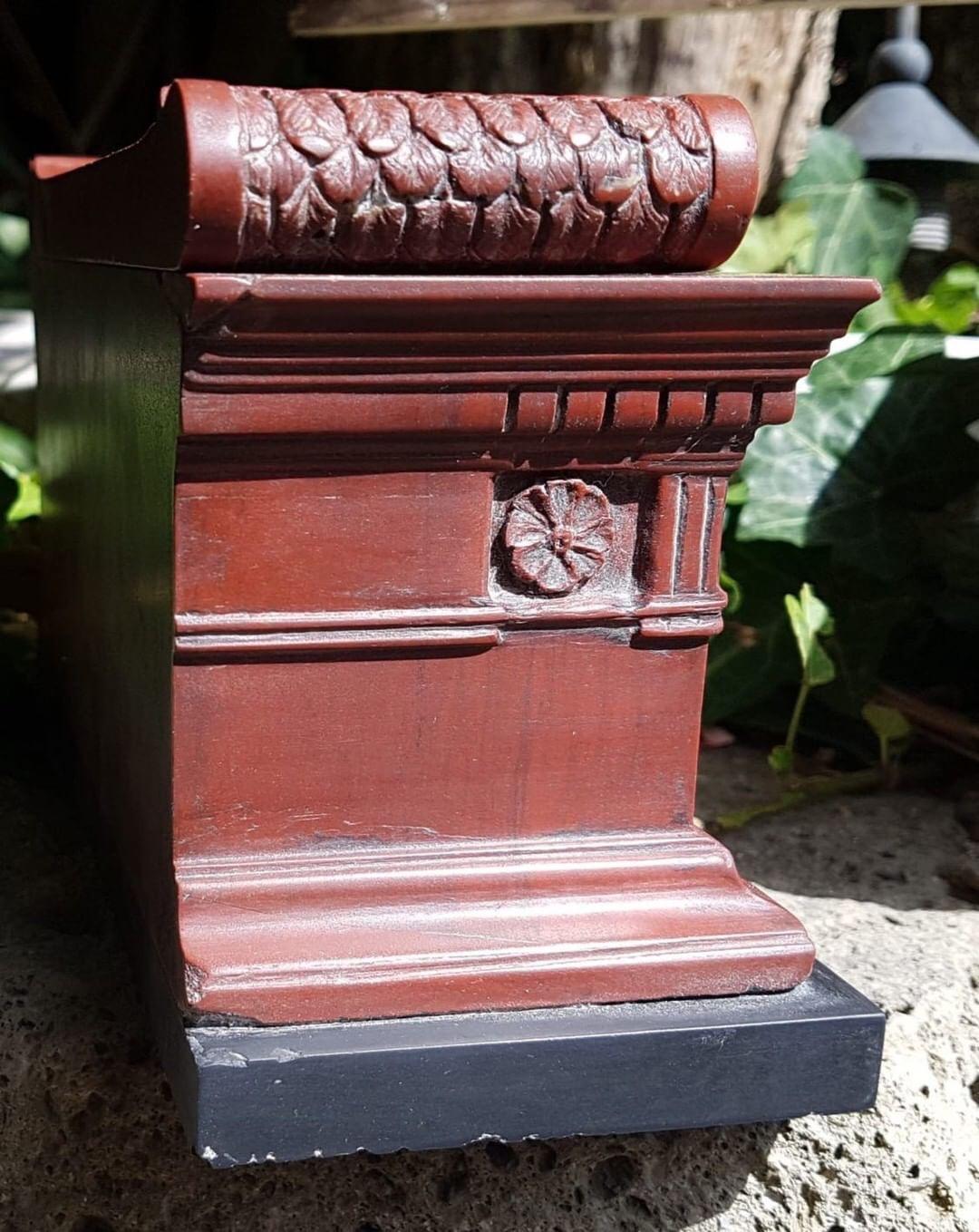 The red marble sarchophagus mounted on a slate base. Removing the top reveals an empty well.