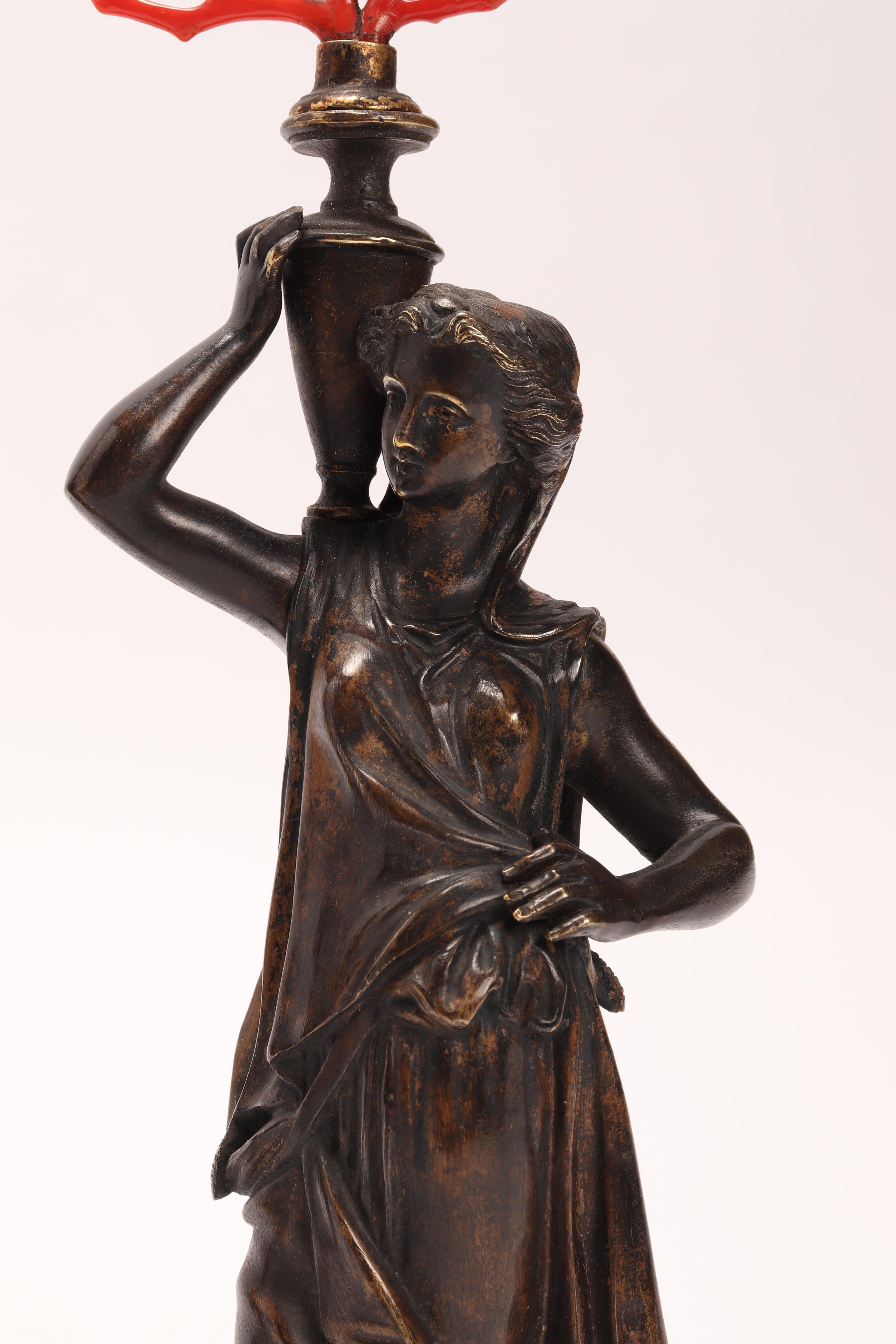 A pair of neoclassical bronze sculptures depicting a woman holding a vase with red Mediterranean coral branches on her shoulder, Italy, circa 1850.