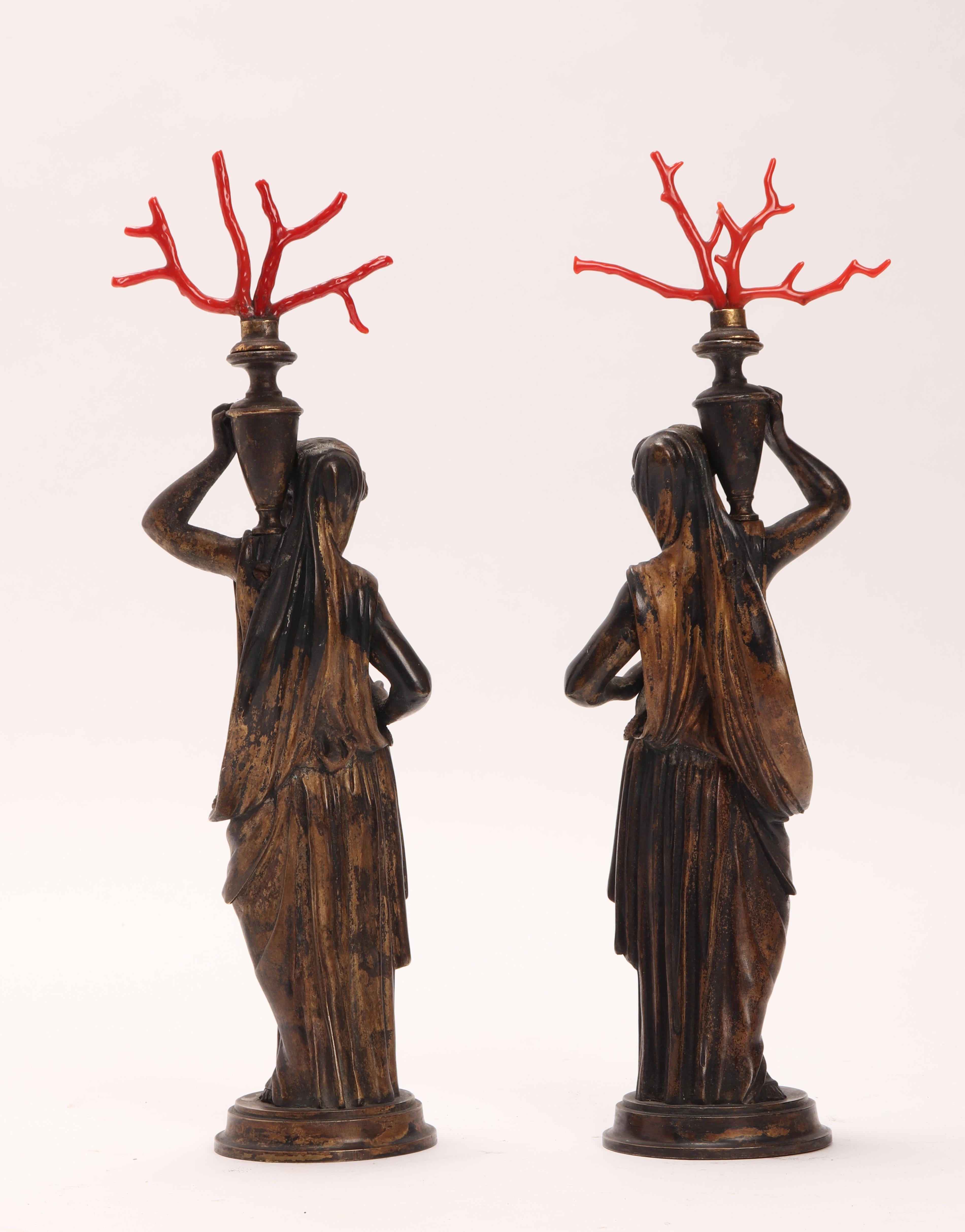 A pair of neoclassical bronze sculptures depicting a woman holding a vase with red Mediterranean coral branches on her shoulder. Italy 1850 ca.