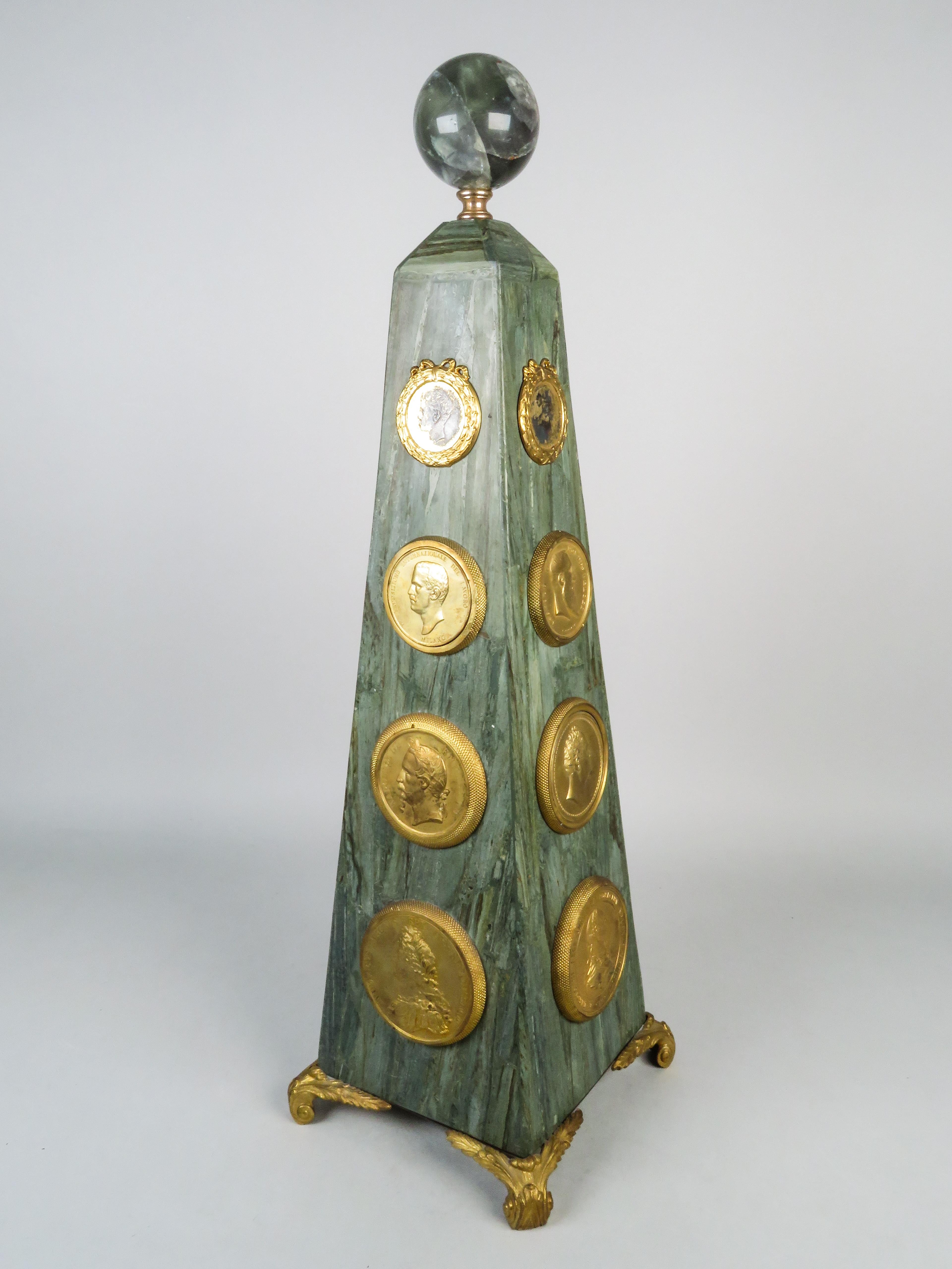 Grand Tour obelisk in marble and gilt bronze topped with a glass sphere and decorated with medallions depicting profiles of European kings and emperors. France, circa 1900.

Dimensions: 57 x 18 x 18 cm