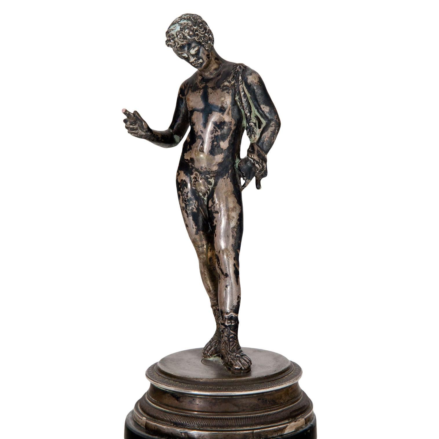 Figure of Narcissus after the famous sculpture in the Museo Nazionale in Naples, standing on a black and beige stone base. Silver, marked at the base. The stone plinth and the index finger are damaged.