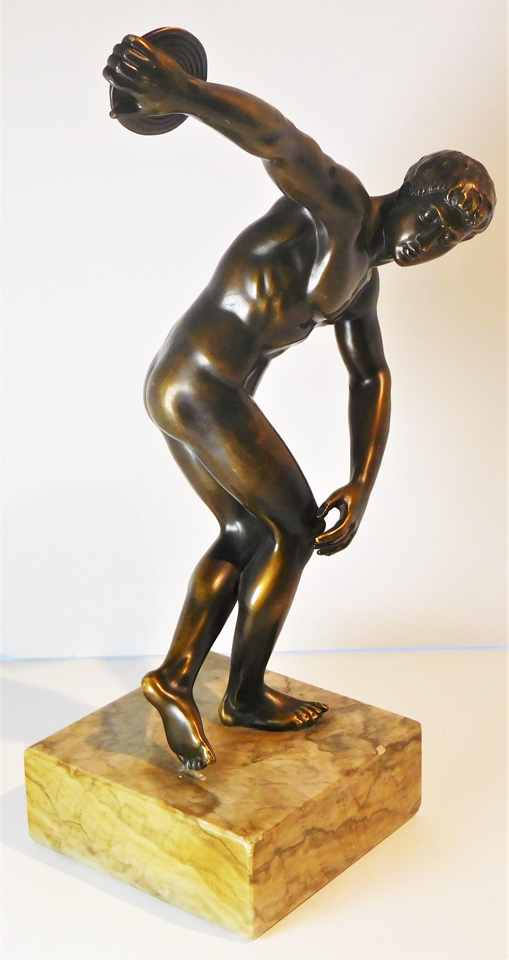 This bronze grand tour souvenir after the classical figure of the discuss throwing athlete by the Greek sculptor Myron, circa 460 BC, has a dark. Mellow, golden brown patina. It is attached to a striated marble plinth base by a recessed flat head