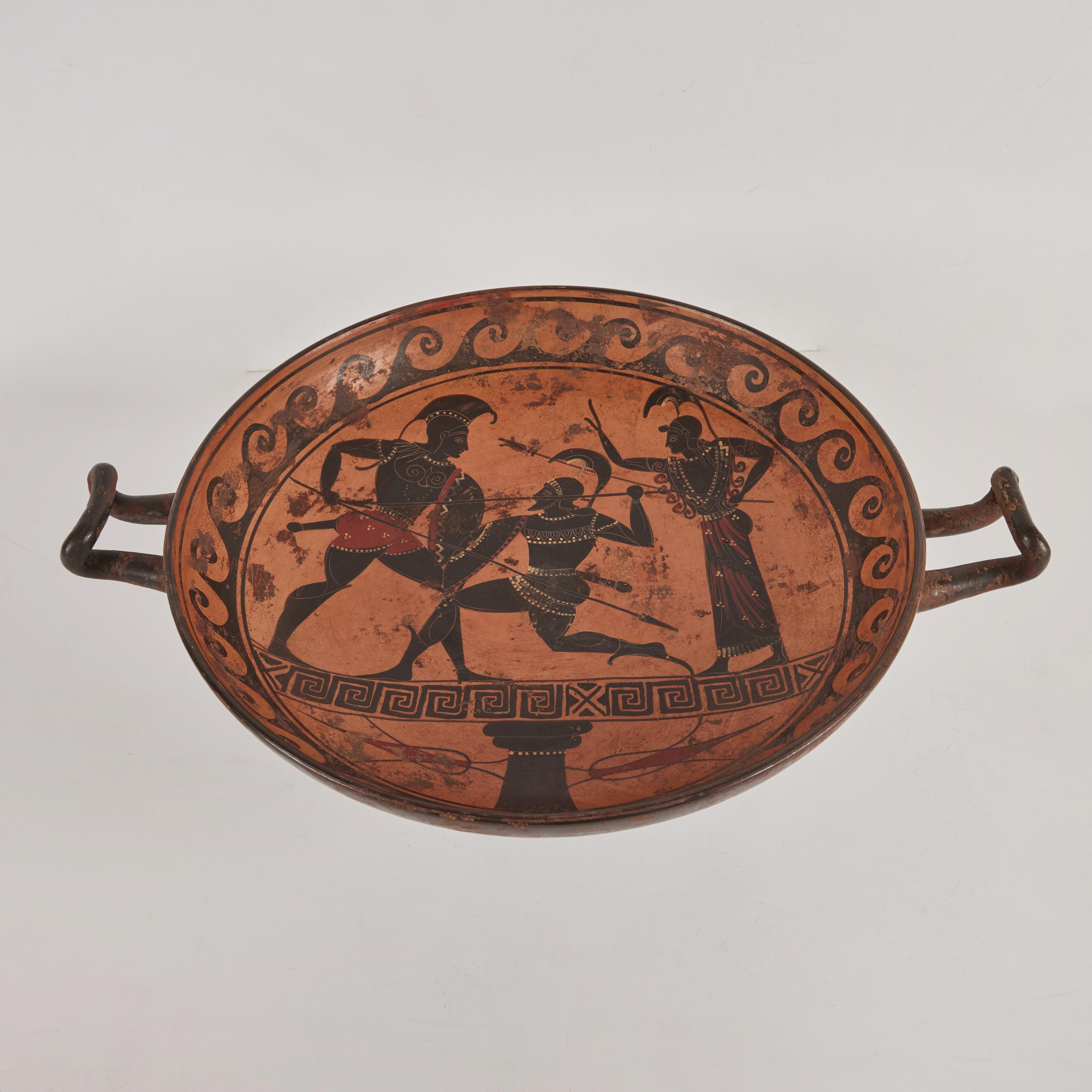 This Grand Tour terracotta drinking cup (kylix) is a later example of the elaborately painted vessels used during symposia in ancient Greece. The broad, shallow bowl with two handles atop a pedestal base permitted the drinker to maintain a recumbent
