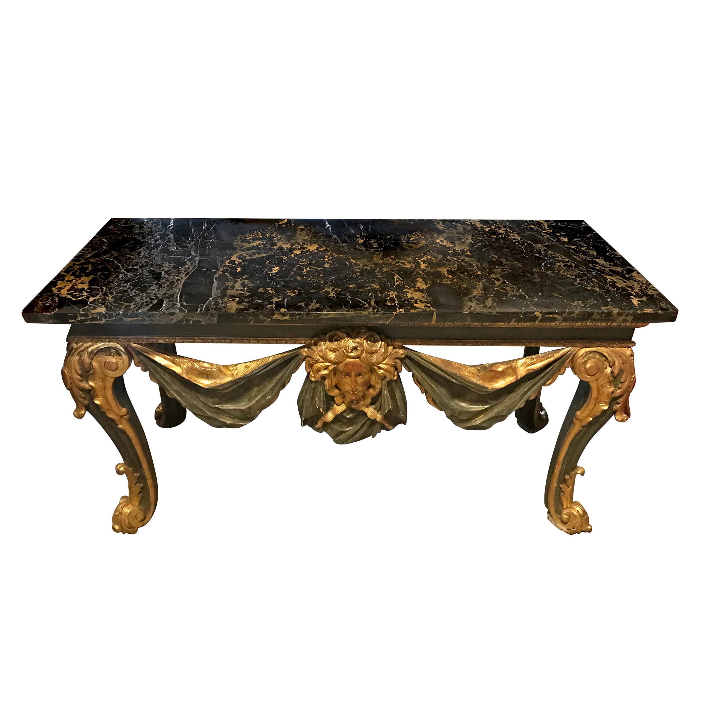 A grand 19th century Italian marble-top console table with an apron carved of wood to mimic a swaged cloth and large classical face in the centre, all painted a wonderful museum olive green with water gilt accents. The top is one large piece of Nero