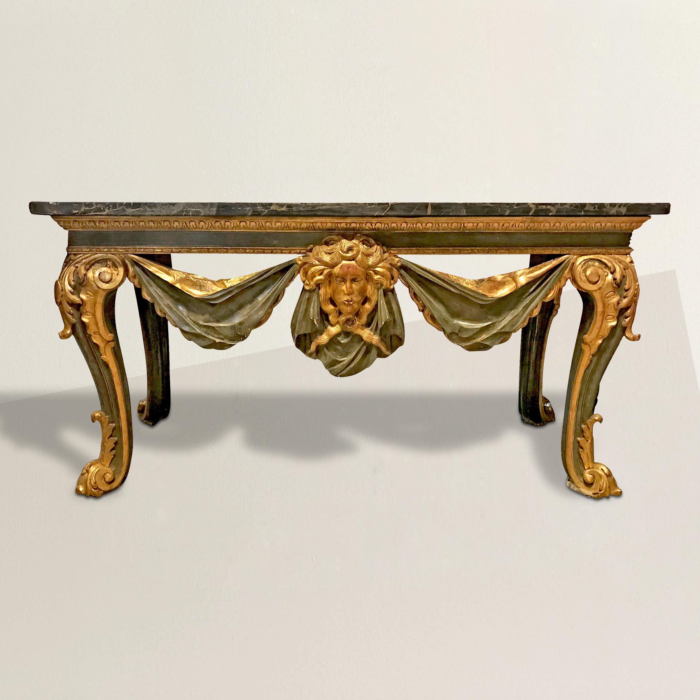 A grand 19th century Italian marble-top console table with an apron carved of wood to mimic a swaged cloth and large classical face in the centre, all painted a wonderful museum olive green with water gilt accents. The top is one large piece of Nero