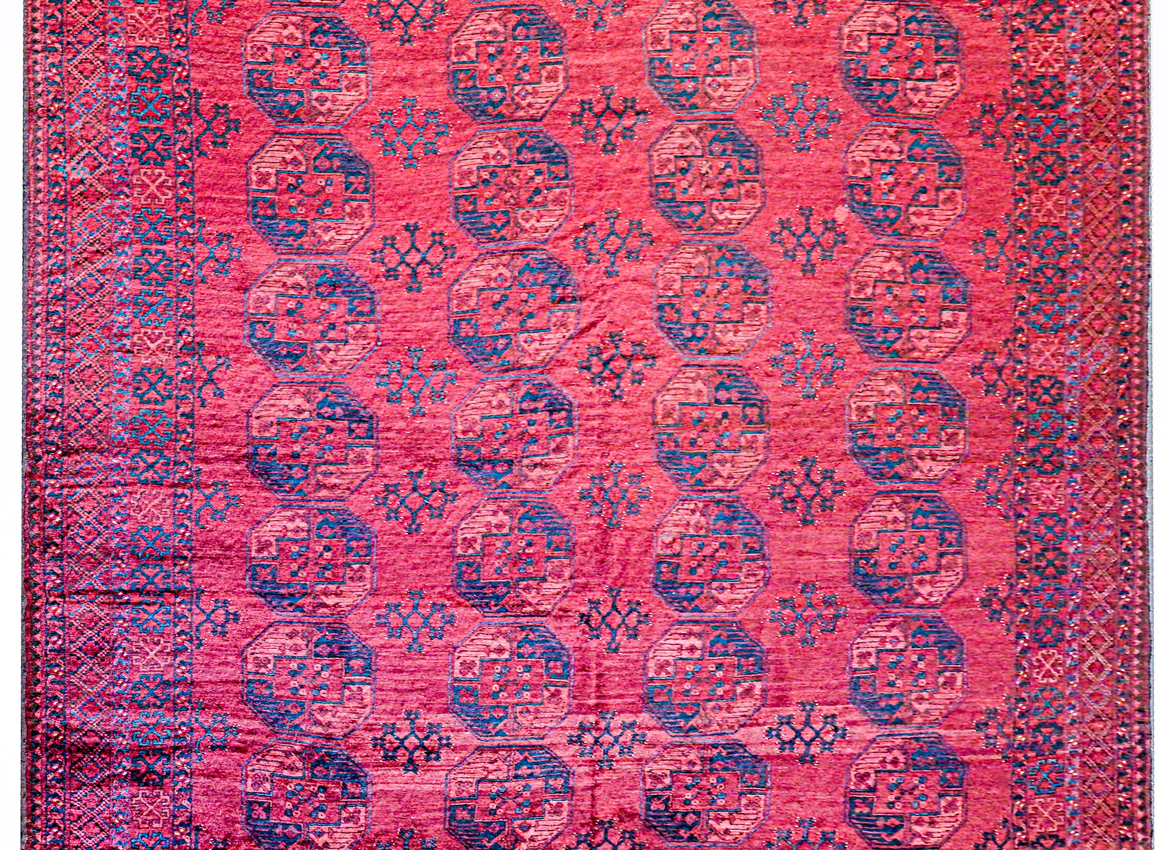 A grand-scale early 20th century Afghani Bashir rug with multiple large octagonal medallions woven in indigo and gold, on a crimson background surrounded by a complementary geometric lattice and stylized floral patterned border.