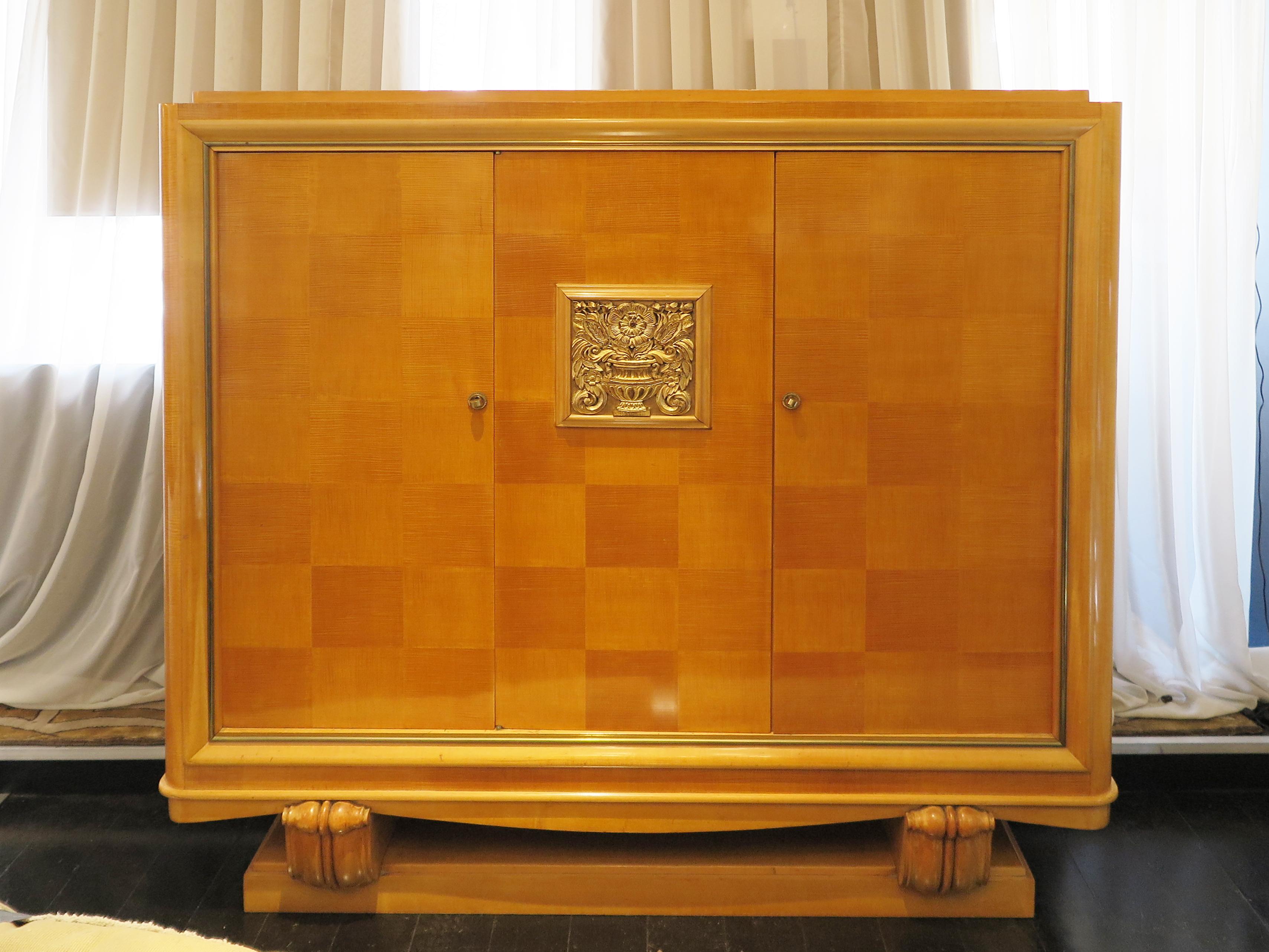 French Art Deco grande Sycamore cabinet attributed to Jean Desnos with floral bas relief detail in gold leaf on center panel.  The cabinet doors showcase a stunning parquetry pattern with a gold leaf detail around the border.   The base features two