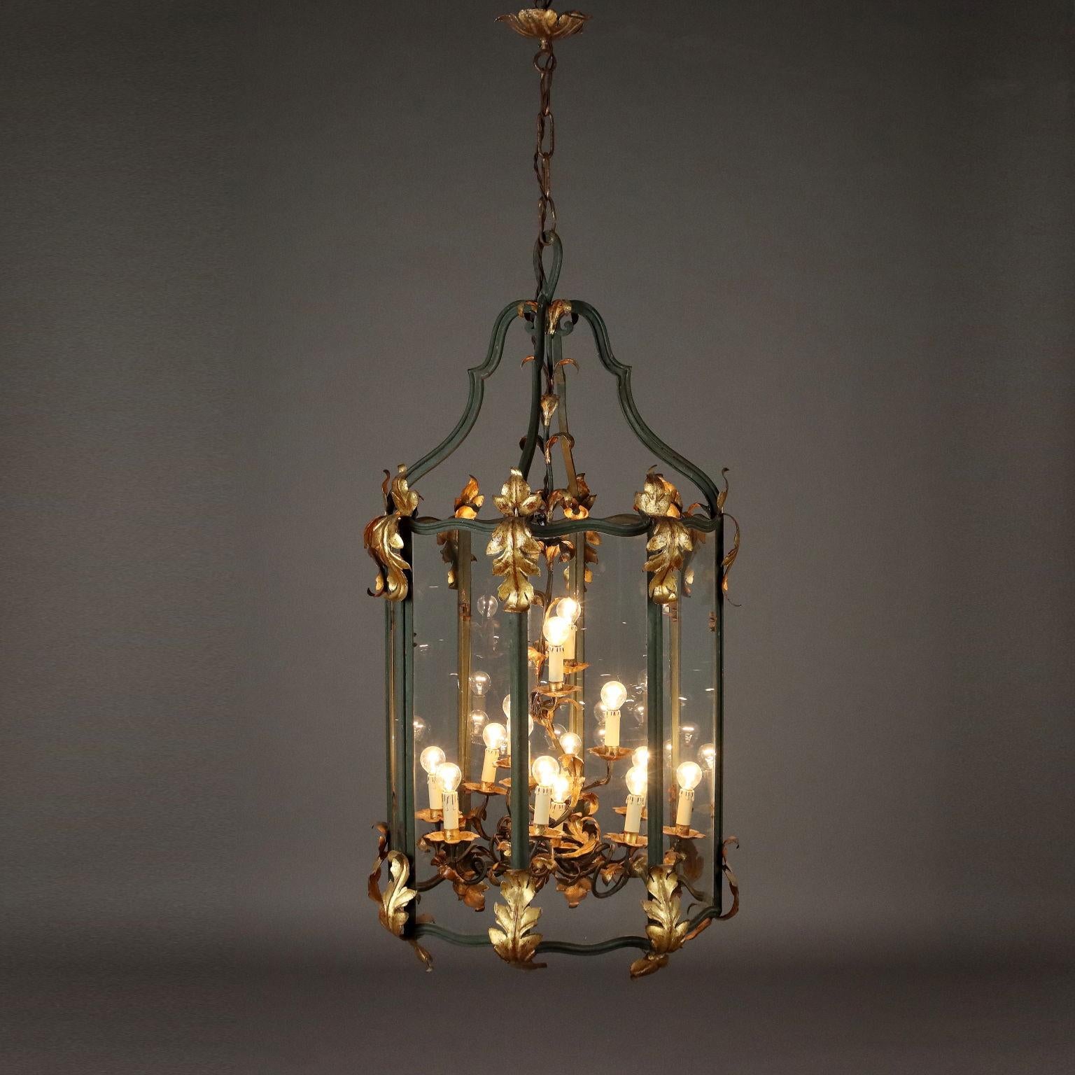 Grande lanterna in ferro laccato e vetro a sezione ottagonale, impreziosita da decori fogliacei in lamierino dorato. Corpo centrale a quattordici luci in ferro battuto, bobeche e decori fogliacei in lamierino dorato.
Italia, inizio XX Secolo.