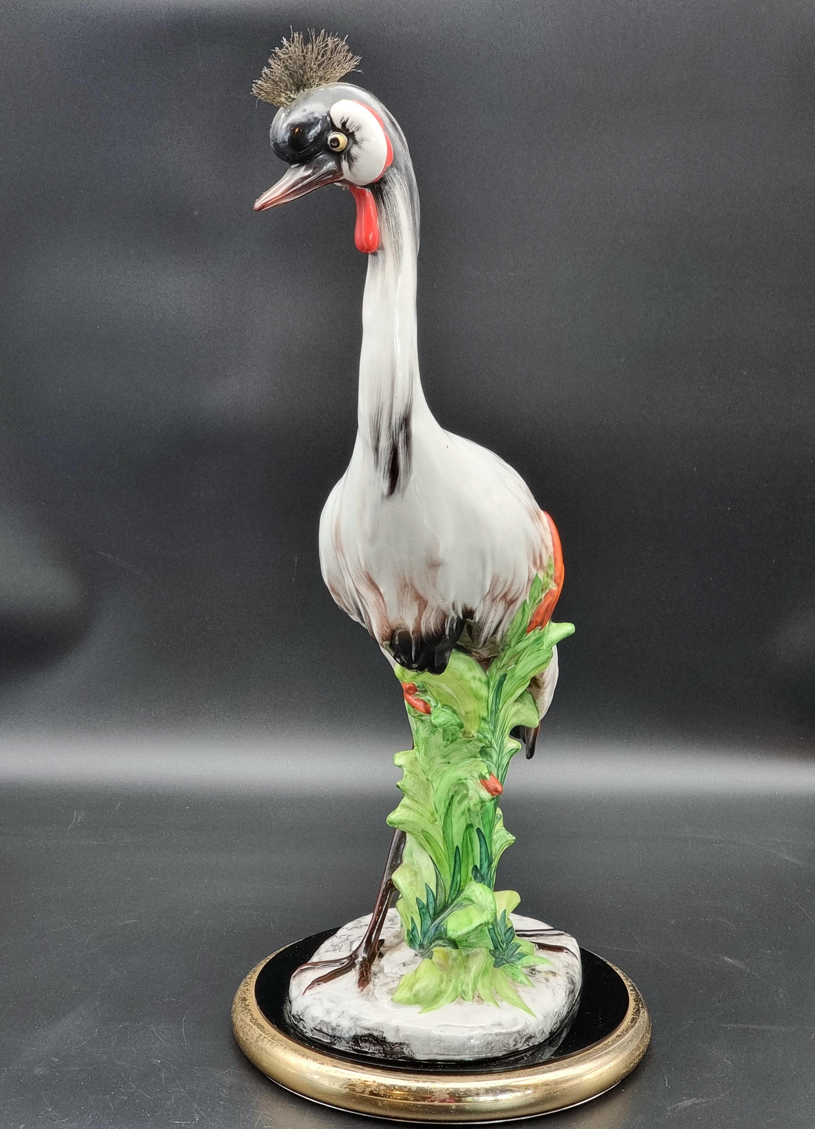 Gran escultura de cerámica vidriada que representa una grulla coronada, ejecutada con considerable habilidad, probablemente en la década de 1950. El ave está representada con gran naturalidad y atención a los detalles anatómicos: la característica