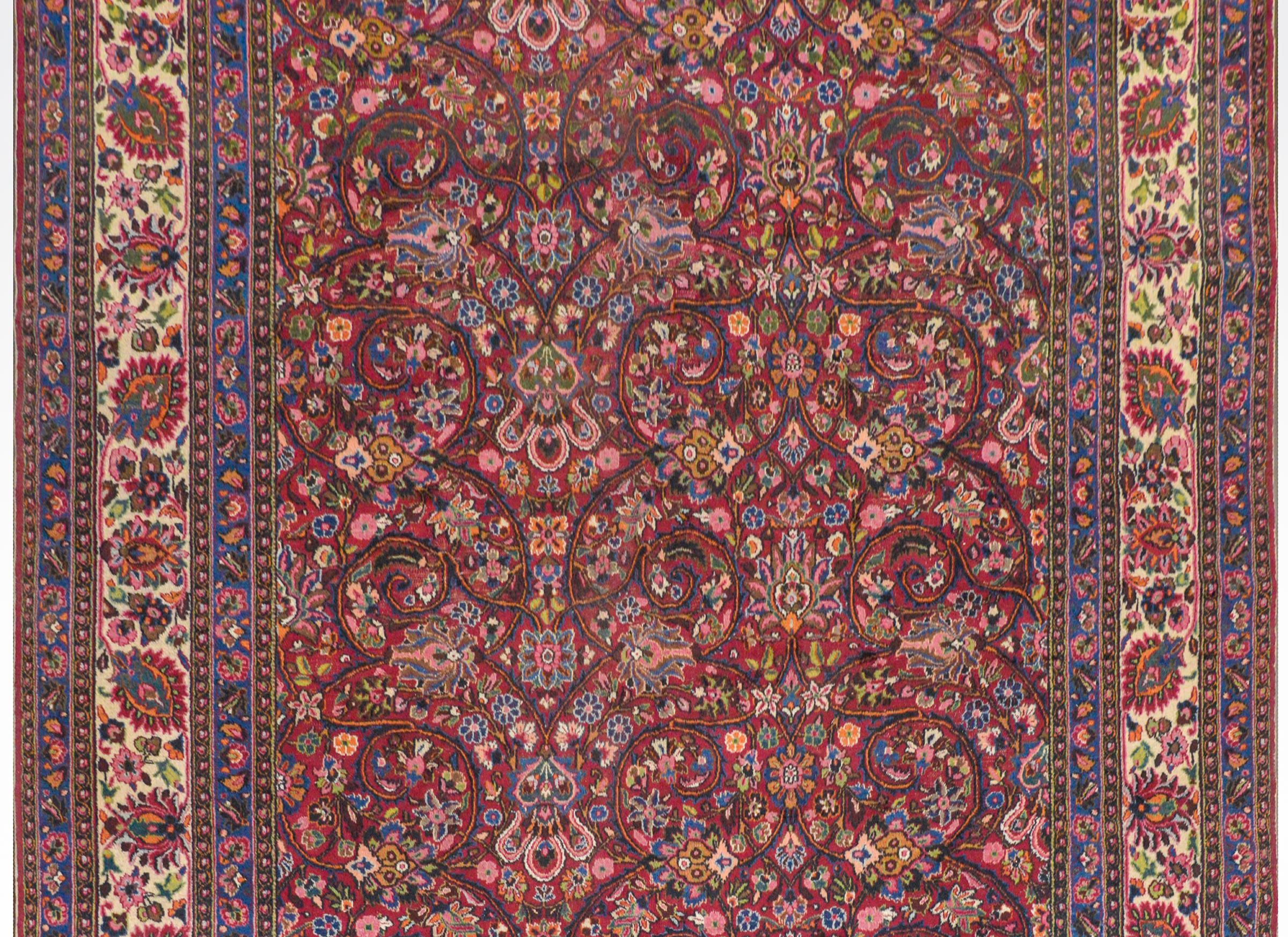 A Grande vintage Persian Mashad with wonderful all-over floral and scrolling vine pattern woven in myriad colors on a dark crimson background. The border is composed of multiple floral patterned stripes flanking a wide white central stripes with a
