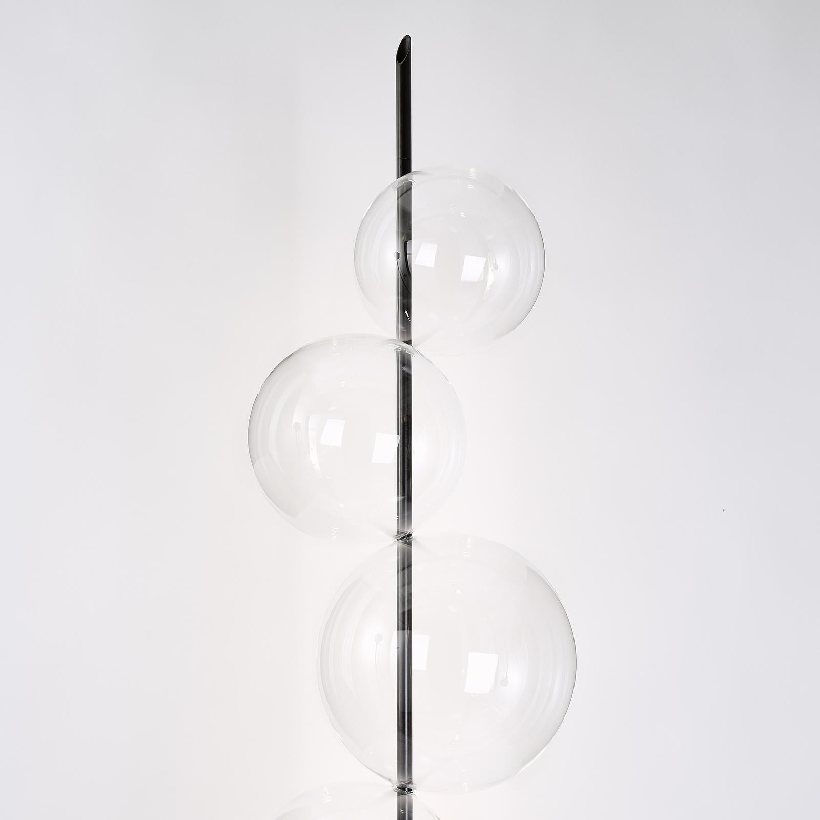 Ce superbe lampadaire se compose de cinq sphères en verre transparent de différentes tailles assemblées sur un poteau cylindrique et une base en laiton bruni, pour former une Silhouette organique abstraite rappelant les grappes de bulles de savon.