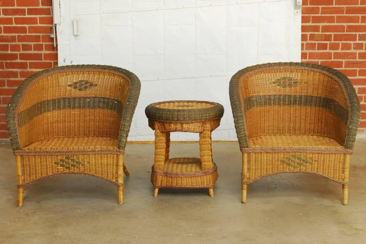 Stylish pair of French wicker and rattan club chairs with side table made in the manner and style of Grange. Art Deco period chairs having a barrel back design constructed from rattan frames covered with wicker and decorated with green and red