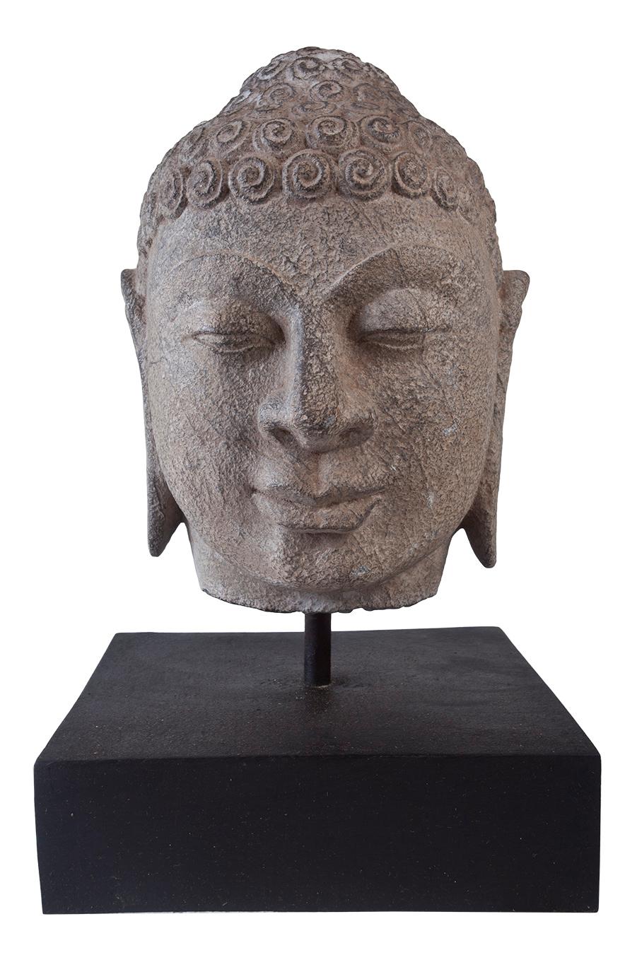 A lovely granite Buddha head on wooden base, early 1900s, India Features include the typical curled hair, elongated ears, half-closed eyes and serene smile. The Ushnisha crown depicts the wisdom and illumination after attaining enlightenment. Just