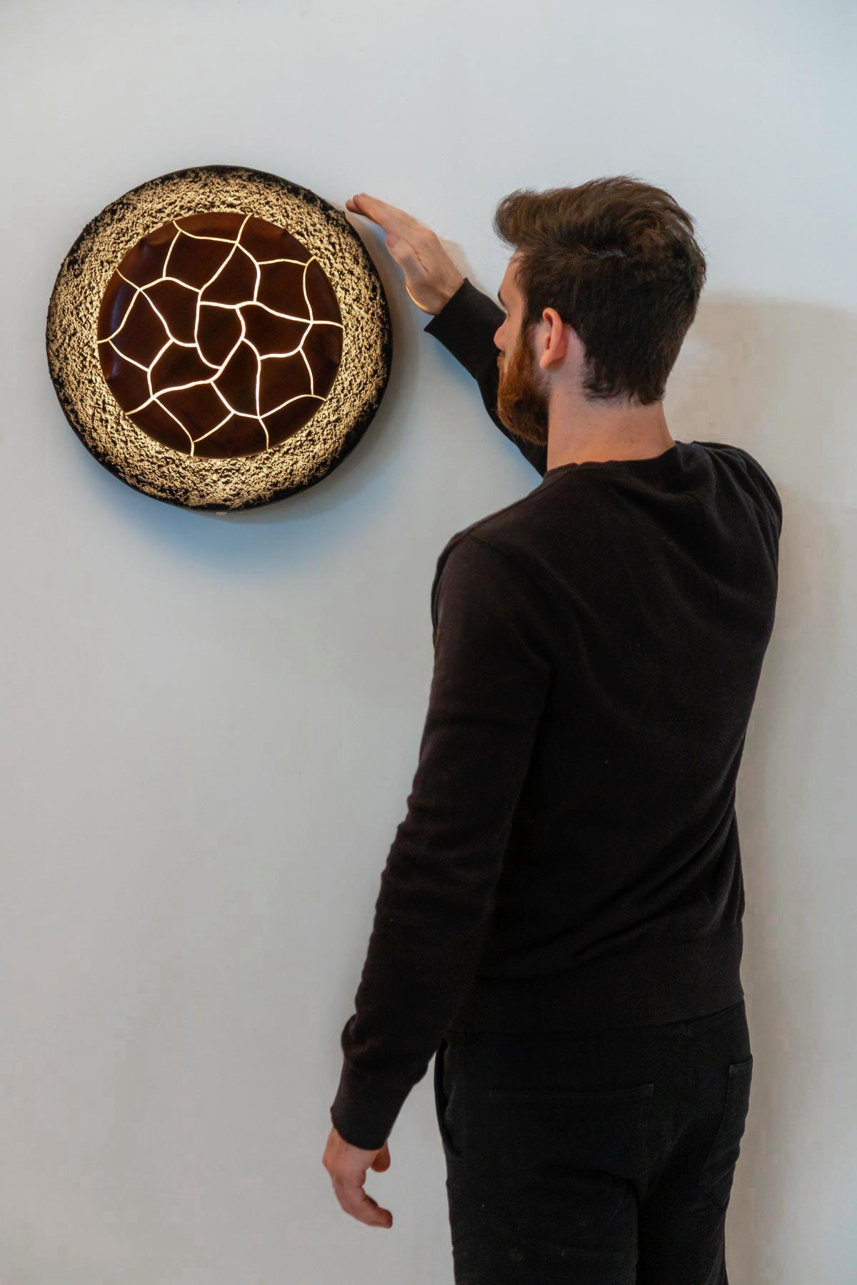 Grão is an illuminated wall sculpture that represents the beauty of transformation.

This work all the composing elements come from the natural and creative marine universe of Marcos Amato.
The base is made from resin-casted sand. A warm light