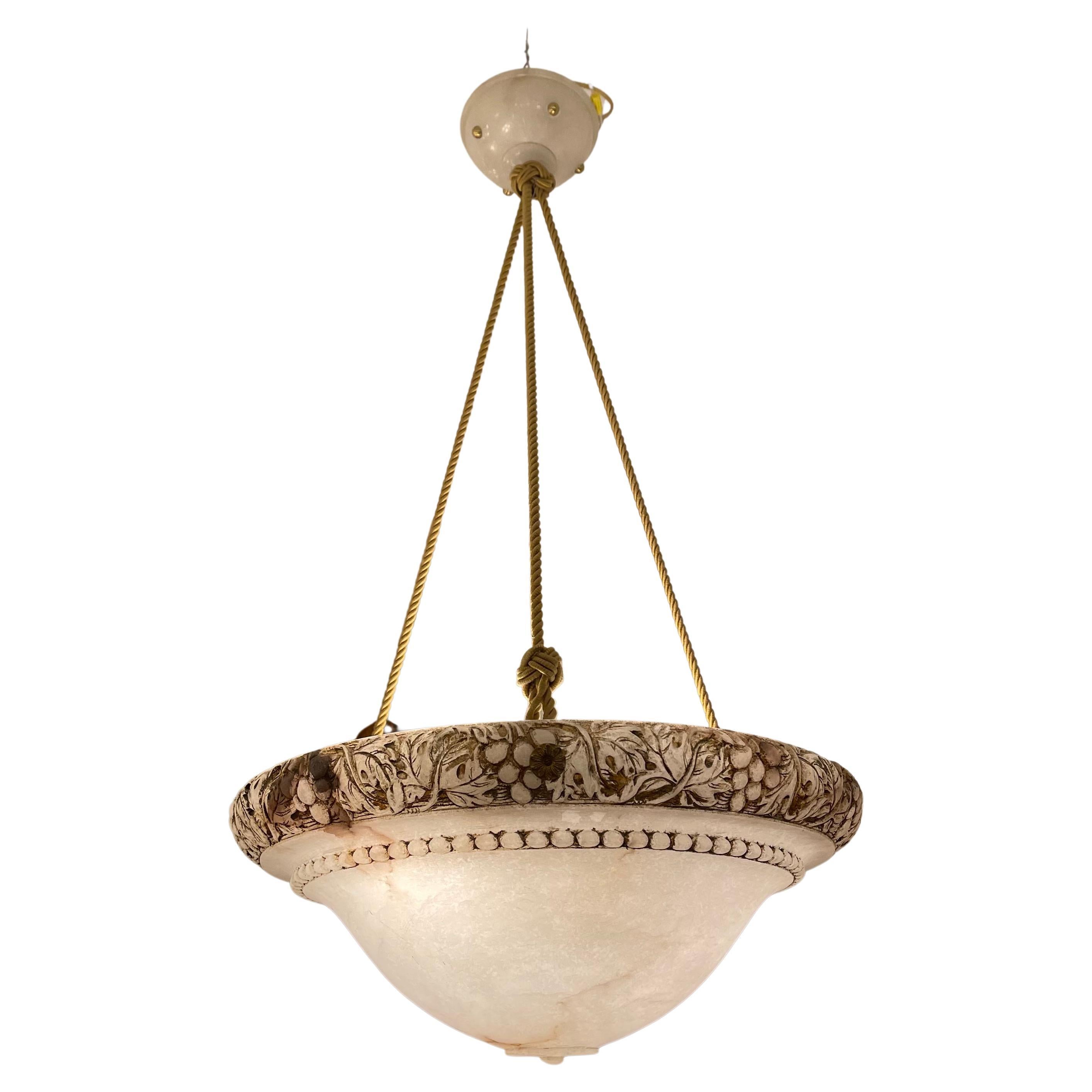 Carved from a single piece of white alabaster stone, this light fixture mounts three bulbs for soft and elegant light diffusion. The electrical wiring is concealed in silk ropes. A neo classical motif of a grapevine is carved in bas-relief on the