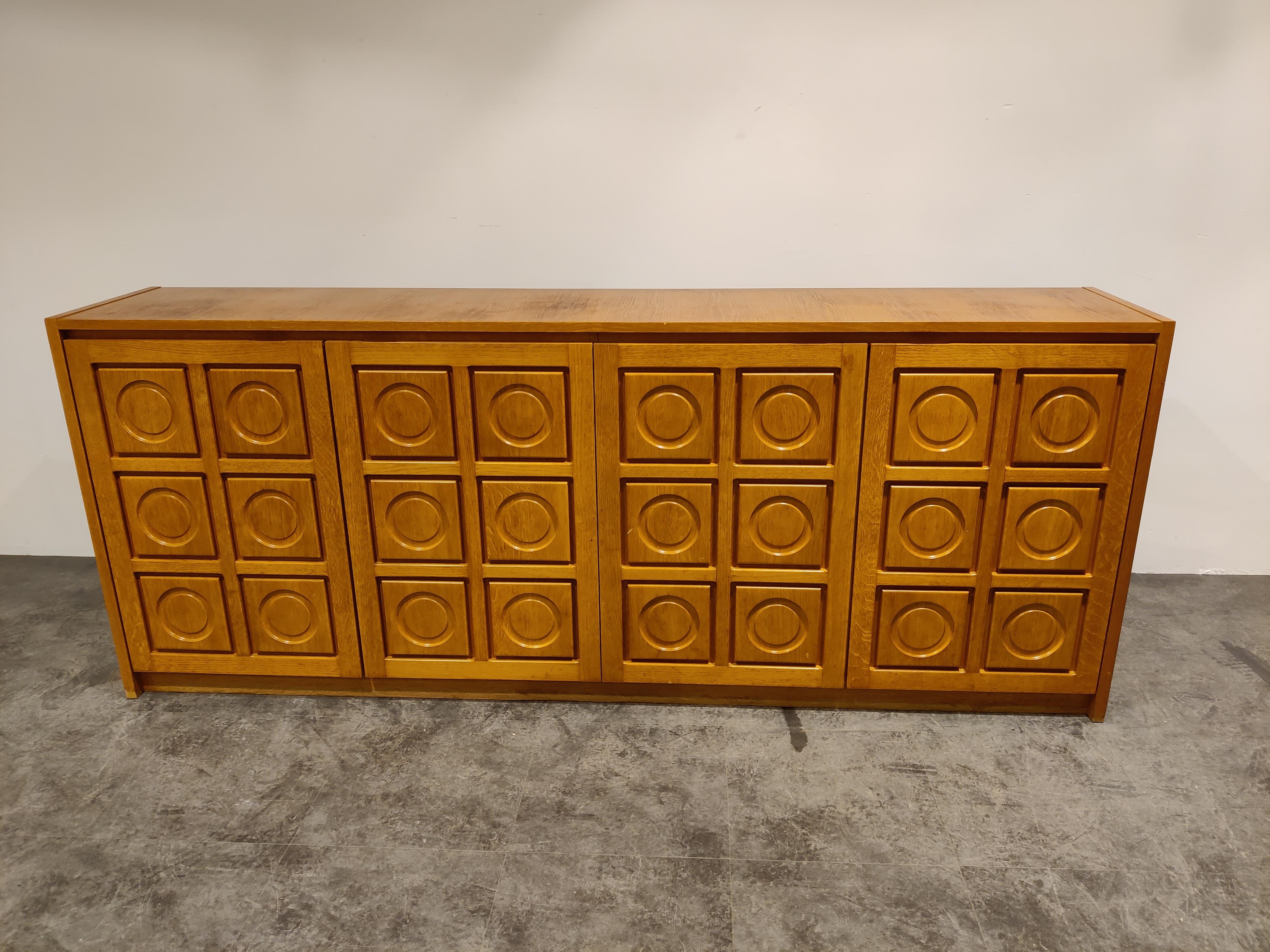 Brown brutalist oak credenza with 4 graphical doors.

Beautiful timeless design and a real eye catcher for your living room.

This credenza provides plenty of storage space with two integrated drawers.

Condition: Good condition with some