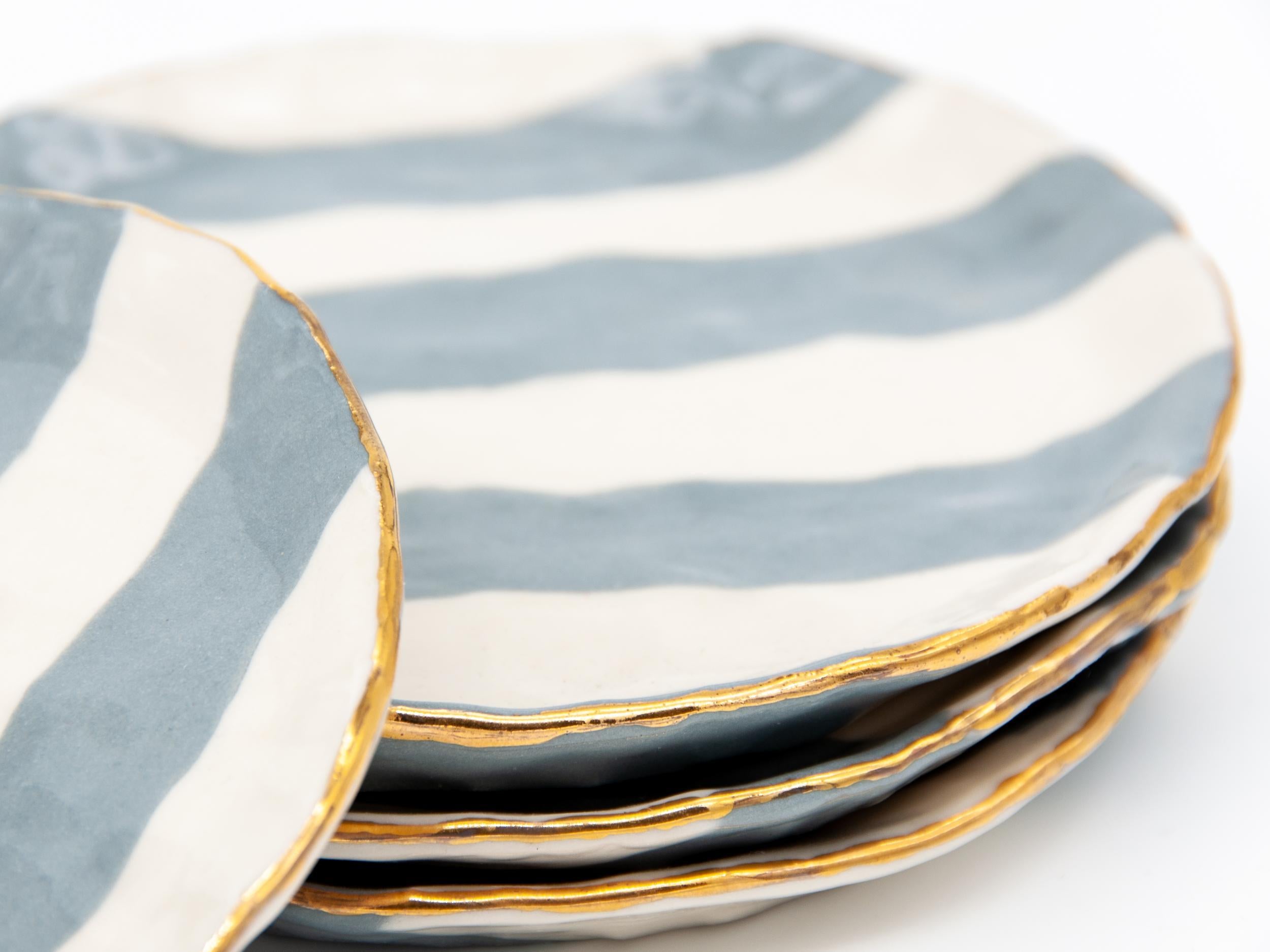 Isabel Halley is a 21st-century ceramic artist based in Brooklyn, NY. She handcrafts all her designs making this set of grey and ivory ribbon plates with gold trim.