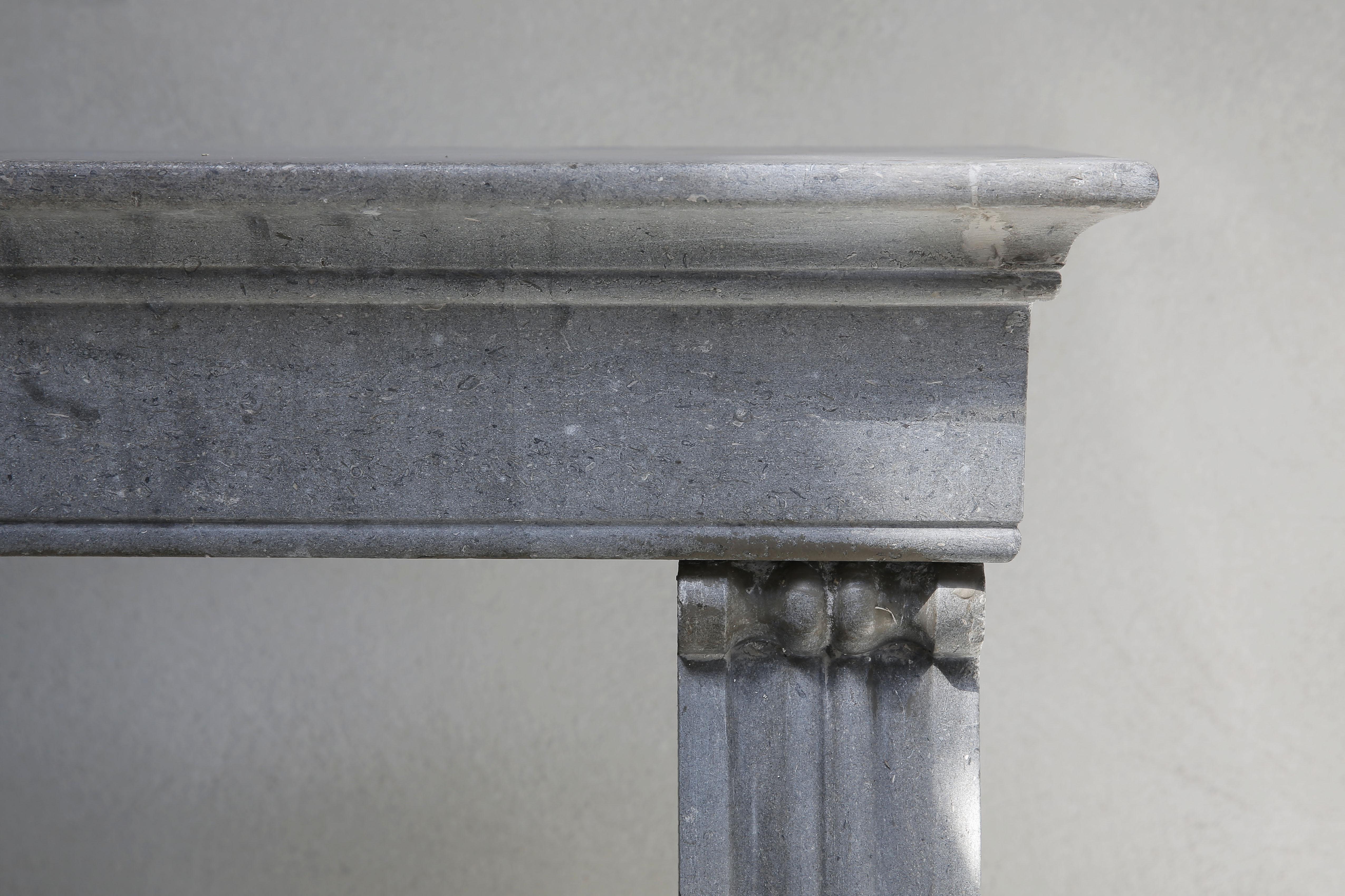 Chic and lightly crafted antique French marble stone fireplace 'Pierre de Besançon'. This grey marble fireplace has a nice look, has a sleek top and slightly curved legs with flutes on the legs. Just above the legs is a nice round operation. A