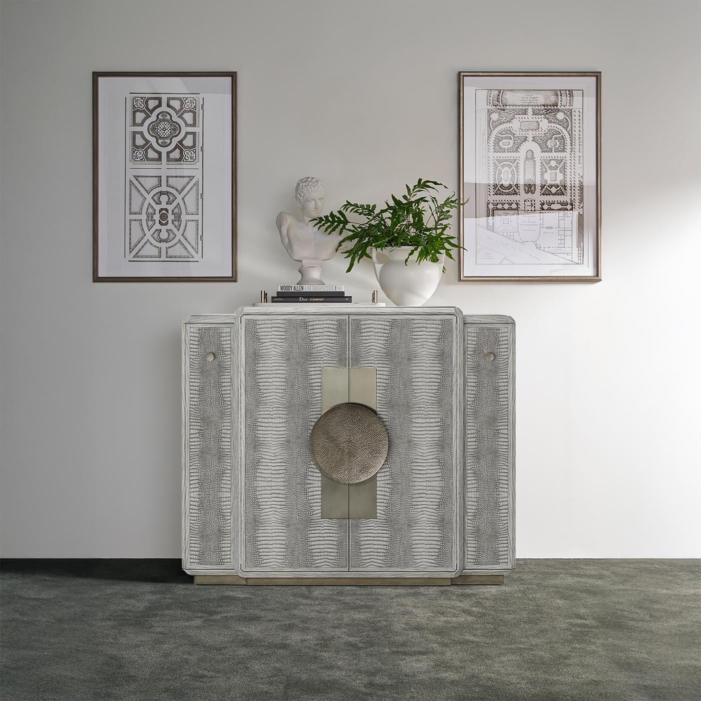 Fabricado en roble y acabado en un rico tono gris argento, este llamativo mueble está adornado con piel repujada de cocodrilo y esculturales herrajes de metal martillado, creando una presencia muy táctil y visualmente cautivadora.

El diseño