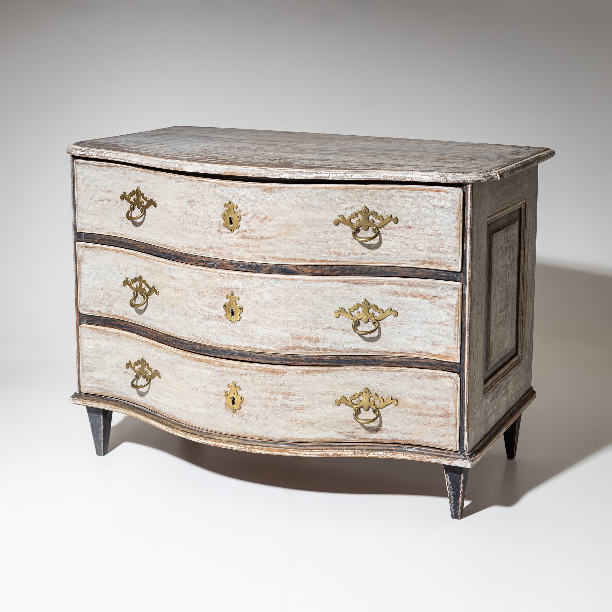 Cassettiera barocca con fronte a serpentina e tre ampi cassetti. I raccordi in ottone forniscono accenti delicati.

La finitura grigia con accenti color antracite è stata applicata di recente e anticata.