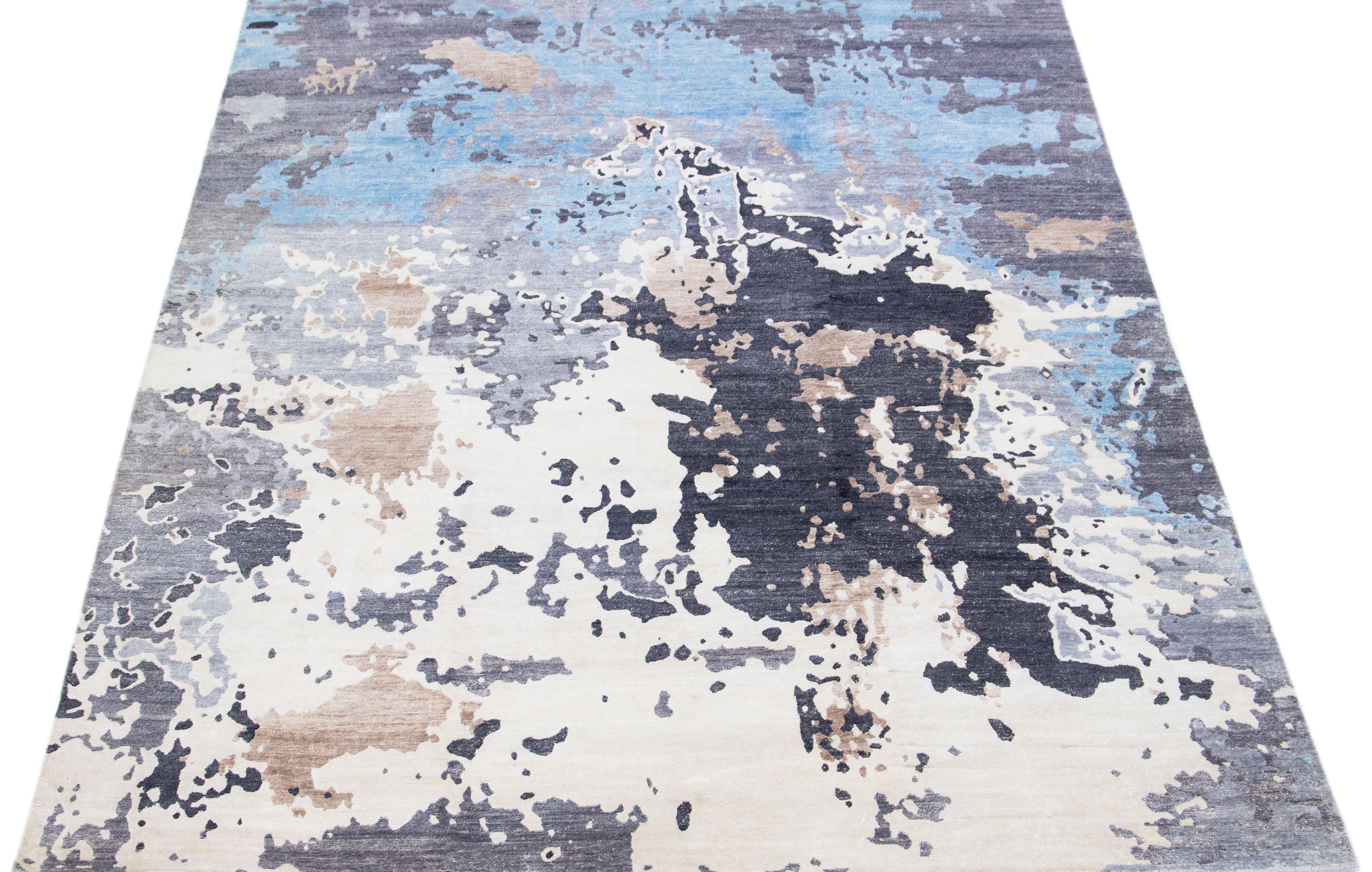 Dieser indische Teppich aus einer Mischung aus Wolle und Seide zeigt ein graues Feld mit einem abstrakten Muster in Blau und Weiß. Seine komponierten Materialien sorgen für Robustheit und Langlebigkeit, während sein ornamentales Design jeden Raum