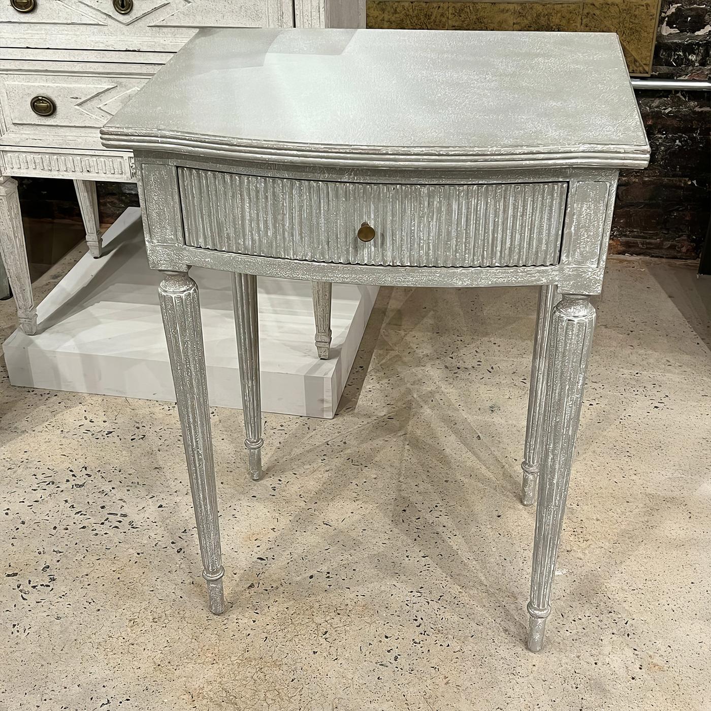  The antique gray finish highlights the table's refined features, including a bow front, a ribbed drawer front and beautifully reeded tapered legs with subtle turnings. Each architectural detail, from the clean-lined top to the fluted columns,