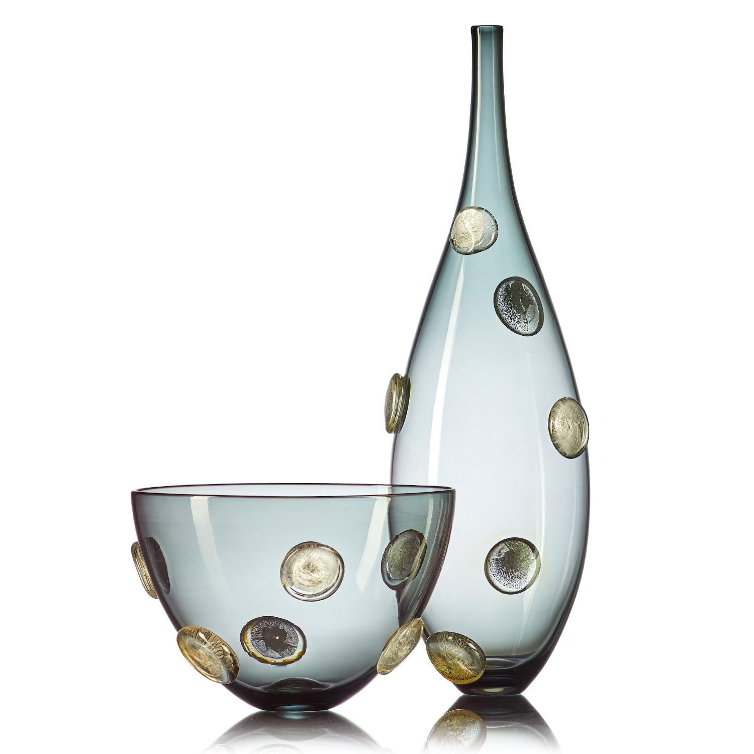 A luminous statement in translucent gray hand blown glass, the Moneto Vessel with Silver Dots features a Cascade of raised metallic coin-shaped dots, encased in clear glass. This large-scale designer vase is hand blown from start to finish by Vetro