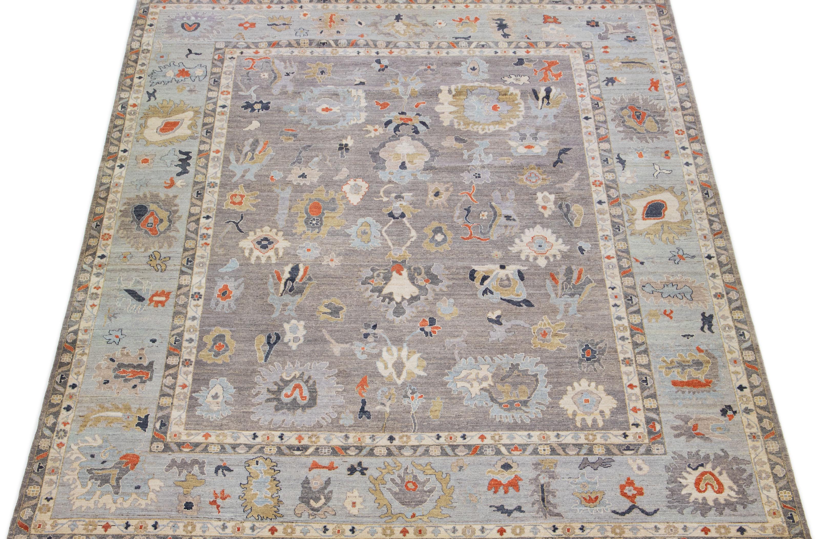 An exquisite oversized Oushak style hand knotted wool rug is presented, showcasing a stunning gray field with a light gray design frame. The rug further highlights rust, blue, and brown accents in a breathtaking floral motif that embellishes the
