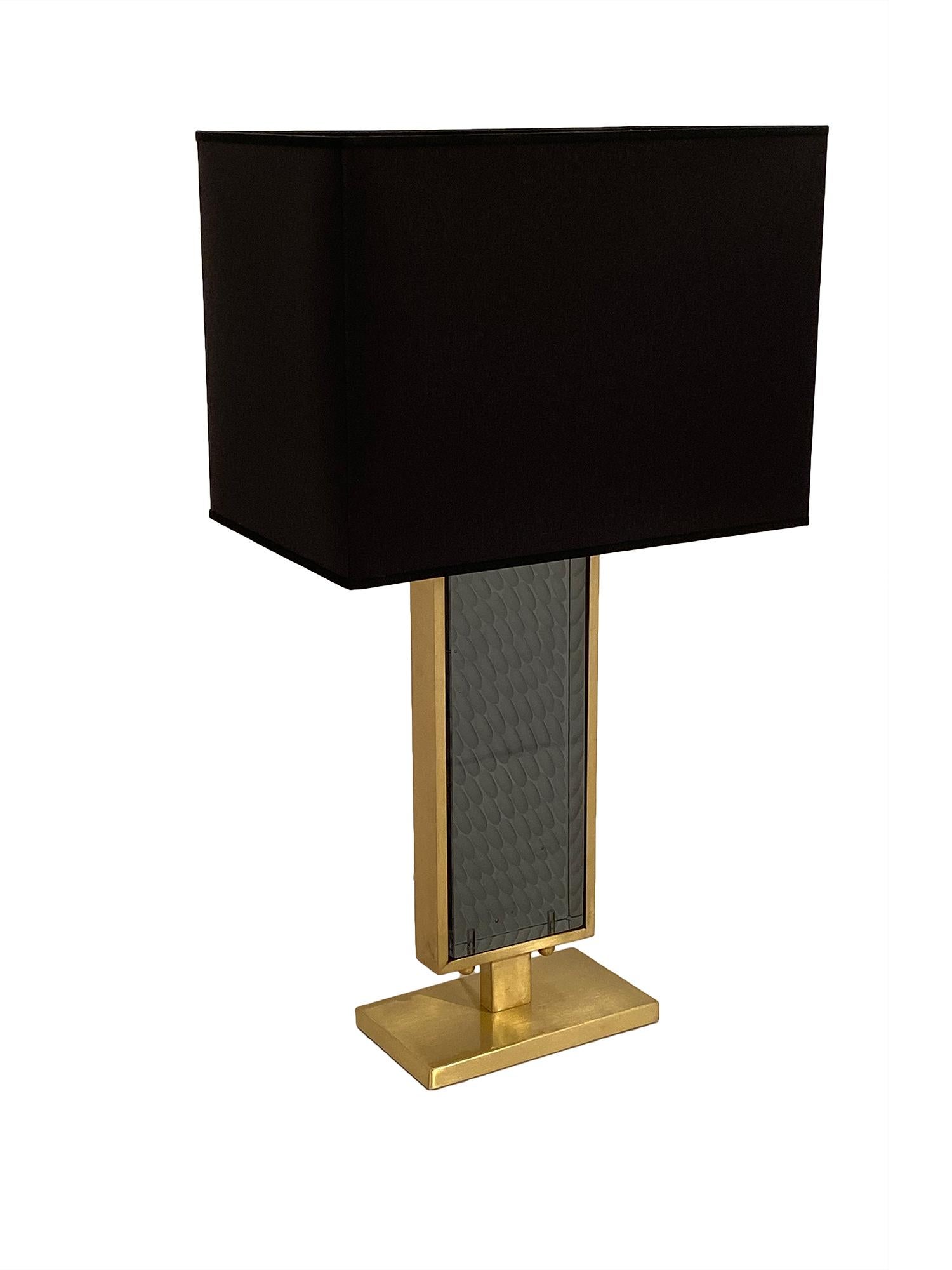 Murano glass in a gray hue and solid brass make this beautiful table lamp so stunning. With a rectangular base, the opaque gray colored glass is surrounded by brass, and light is able to pass through the glass in remarkable ways. The glass is