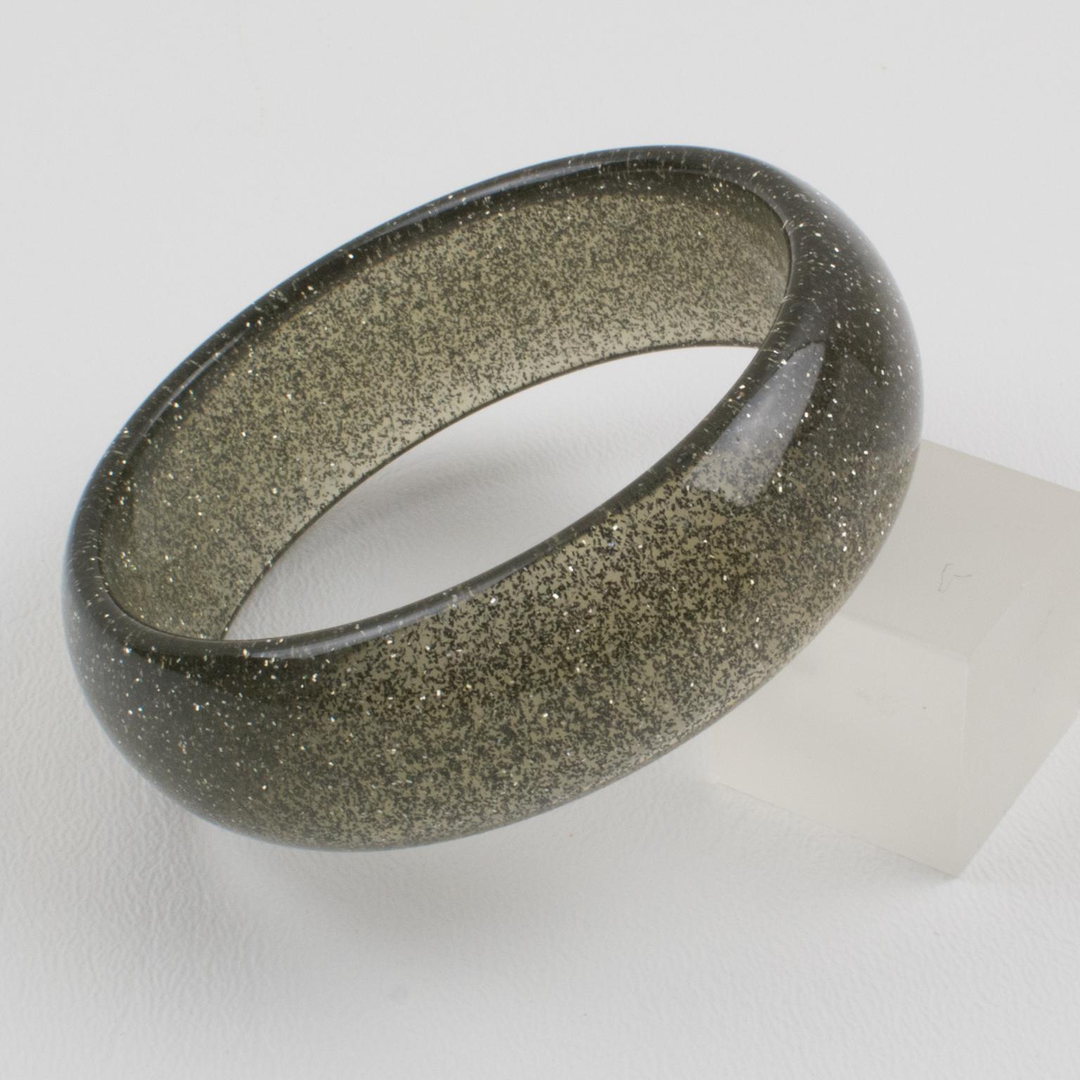 Questo affascinante bracciale bangle in lucite o resina ha una forma a cupola ed è composto da lucite grigia trasparente iniettata con inclusioni di coriandoli metallici in argento. I coriandoli metallici glitterati ricordano le decorazioni