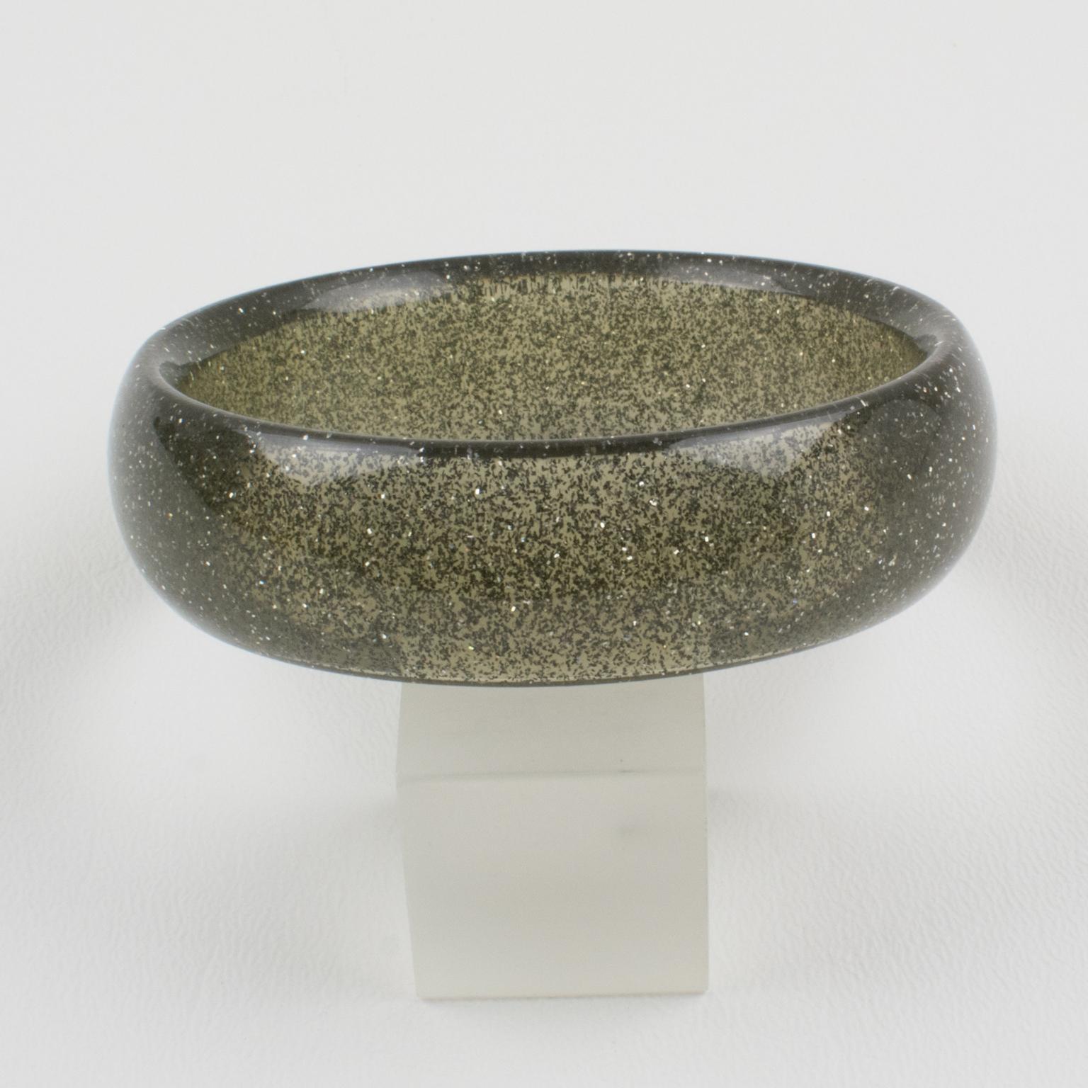 Questo affascinante bracciale bangle in lucite ha una forma a cupola ed è composto da lucite grigio fumo trasparente iniettata con inclusioni di coriandoli metallici in argento. I coriandoli metallici glitterati ricordano le decorazioni natalizie.